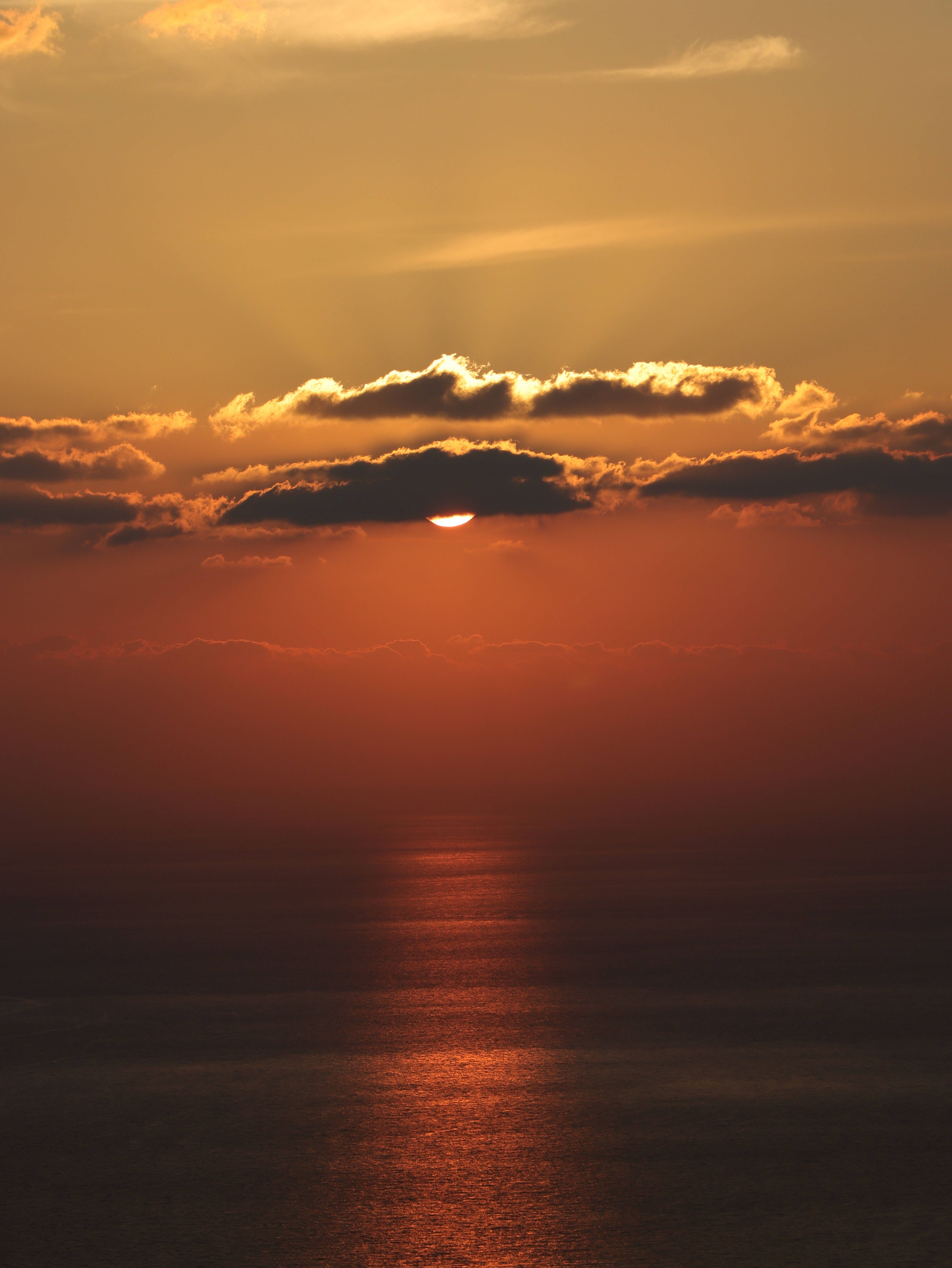 雲朵 桌布 壁紙 — 令人驚嘆的海上日落，金色陽光穿透烏雲，在平靜的水面上反射出熾熱的橙色。