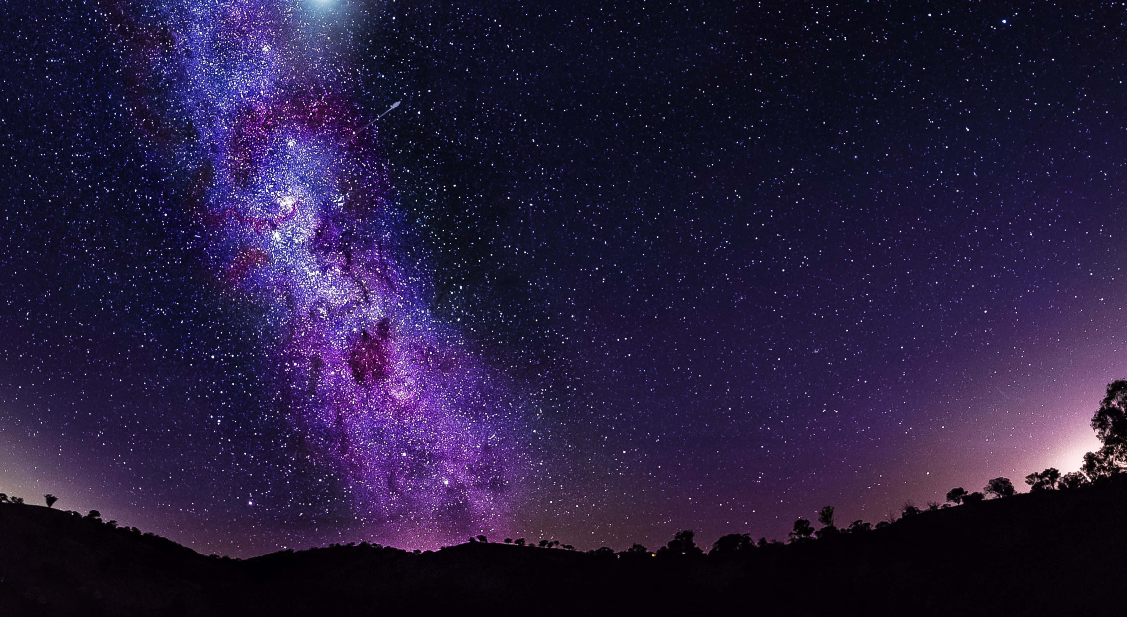 Stars 桌布 壁紙 — 令人驚嘆的銀河系景觀，在黑暗輪廓的山丘上方的星空夜空中，以充滿活力的紫色和藍色色調閃耀。