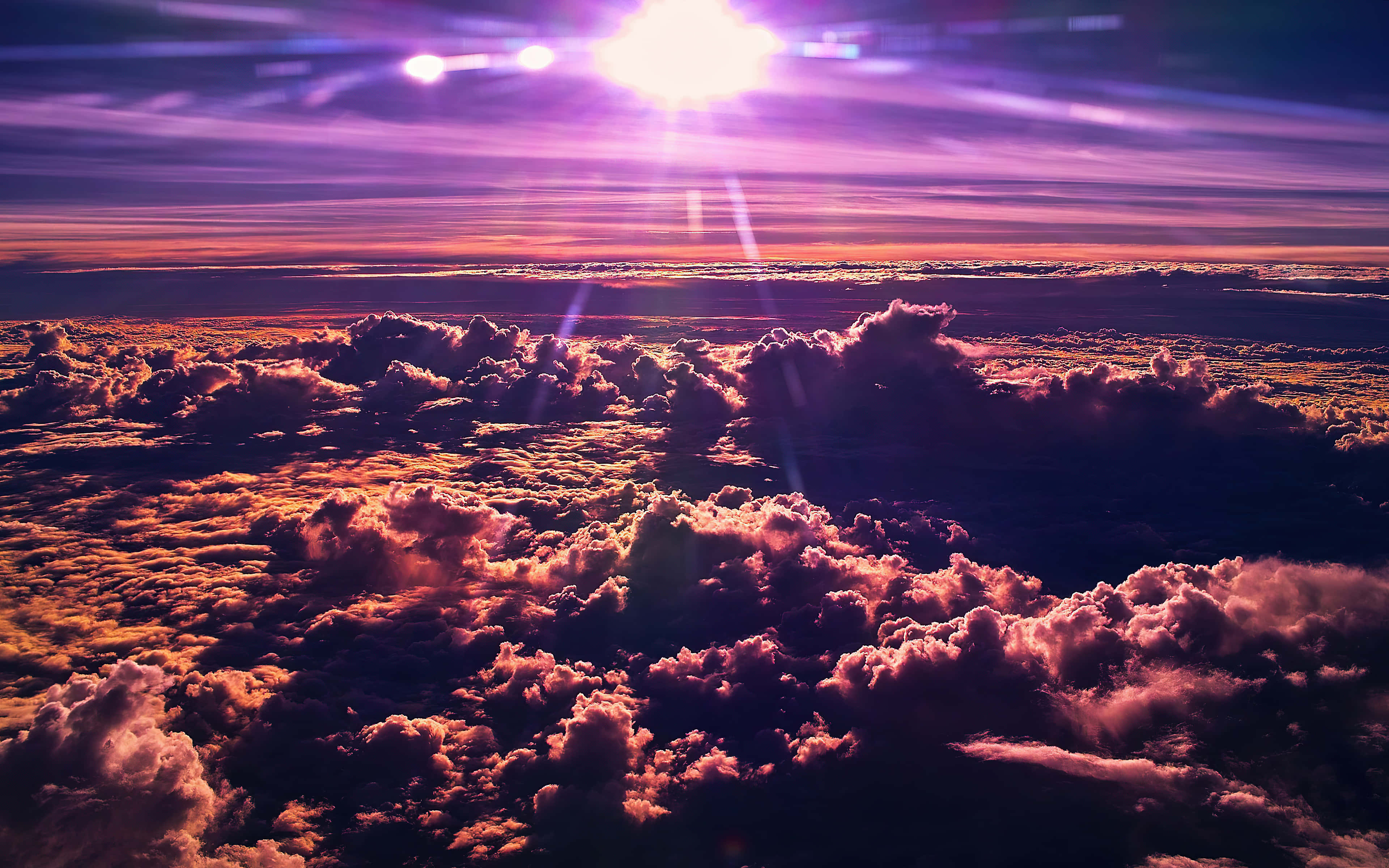 Clouds 4K 桌布 壁紙 — 令人驚嘆的雲層鳥瞰圖，沐浴在鮮豔的紫色和橙色色調中，太陽在頭頂明亮照耀。