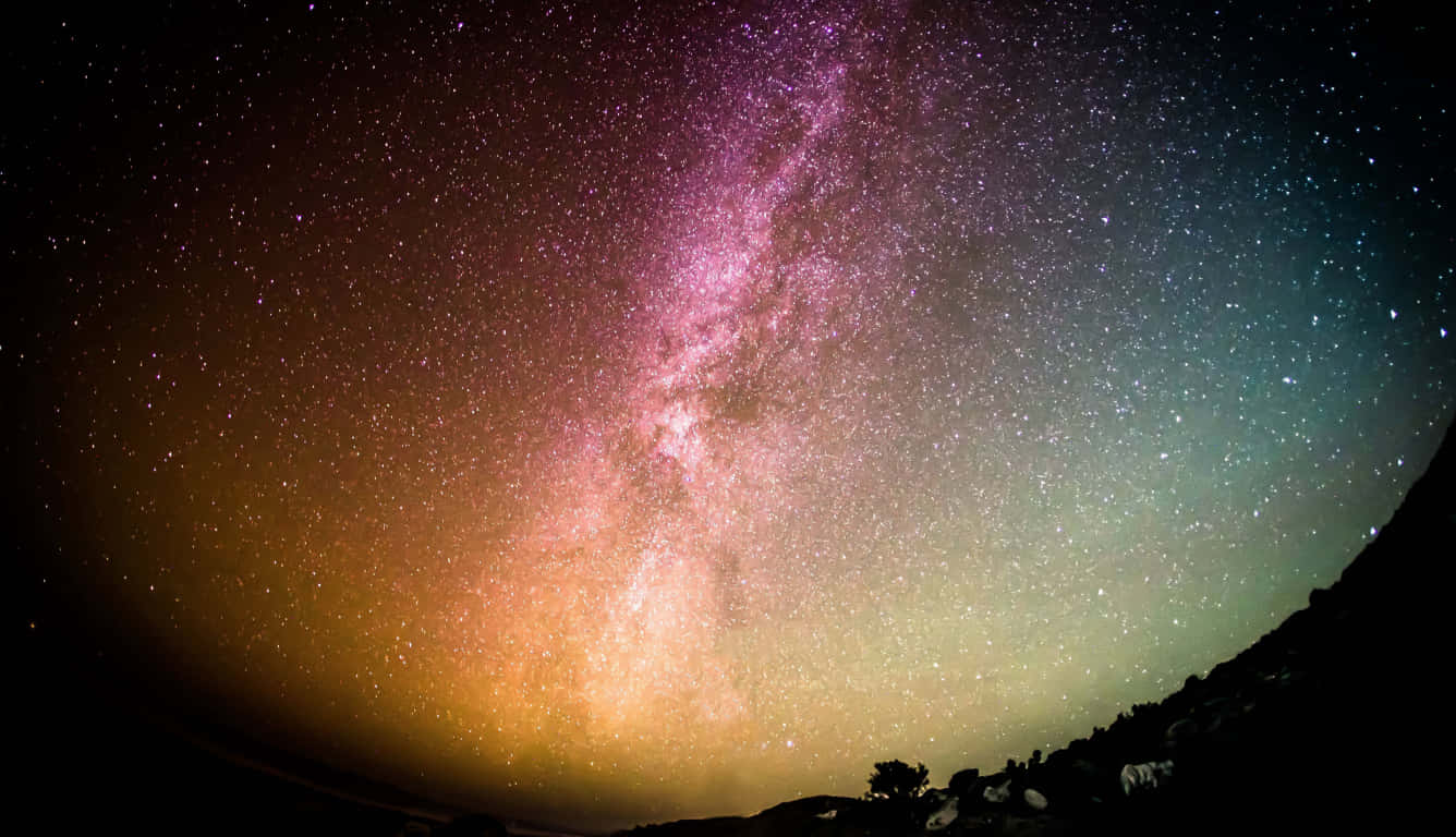Starry Sky 桌布 壁紙 — 令人驚嘆的魚眼視角，銀河系在黑暗山脈剪影上方閃耀著粉紅和金色光芒。