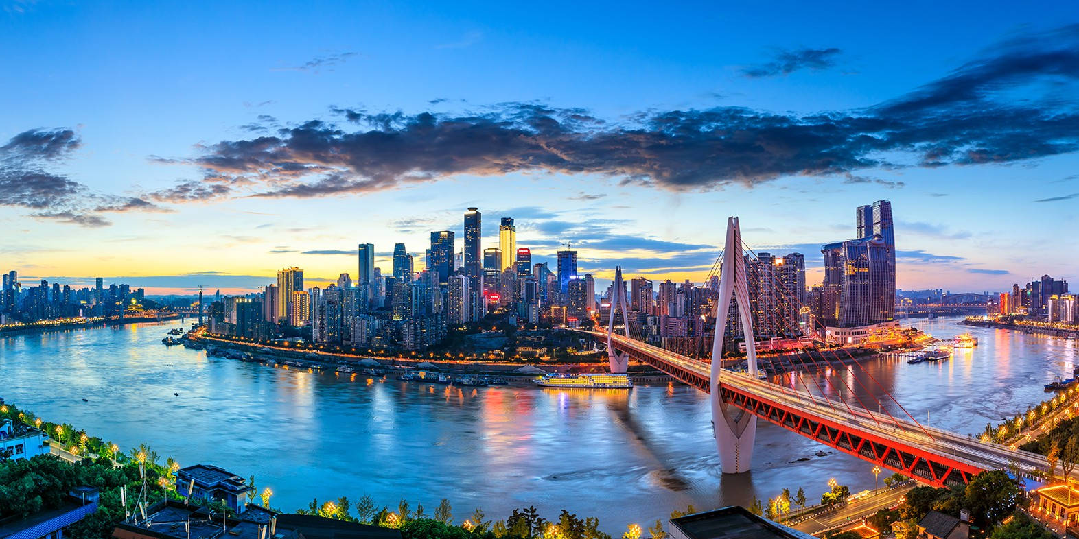 Chongqing 桌布 壁紙 — 令人驚嘆的黃昏城市景觀，一座發光的橋樑橫跨寬闊的河流，倒映著摩天大樓和溫暖的燈光。