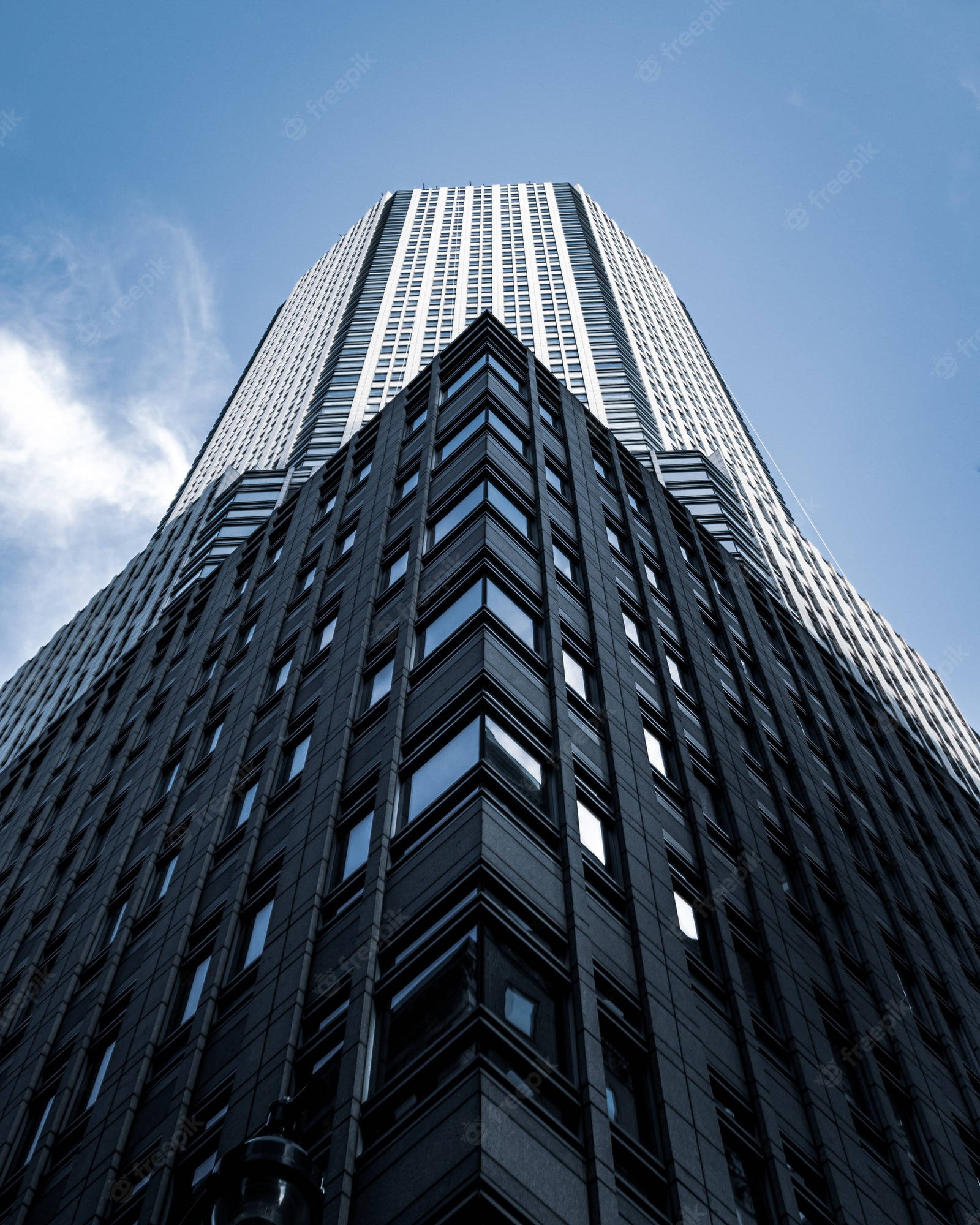 Skyscraper 桌布 壁紙 — 以低角度拍攝一座高聳的現代摩天大樓，深色玻璃窗映襯著晴朗藍天和縷縷白雲。