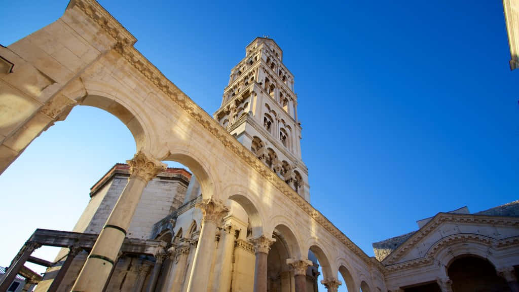 Croatia 桌布 壁紙 — 以低角度觀看一座歷史悠久的石造大教堂，擁有拱形柱廊和高聳的鐘樓，背景是清澈的藍天。
