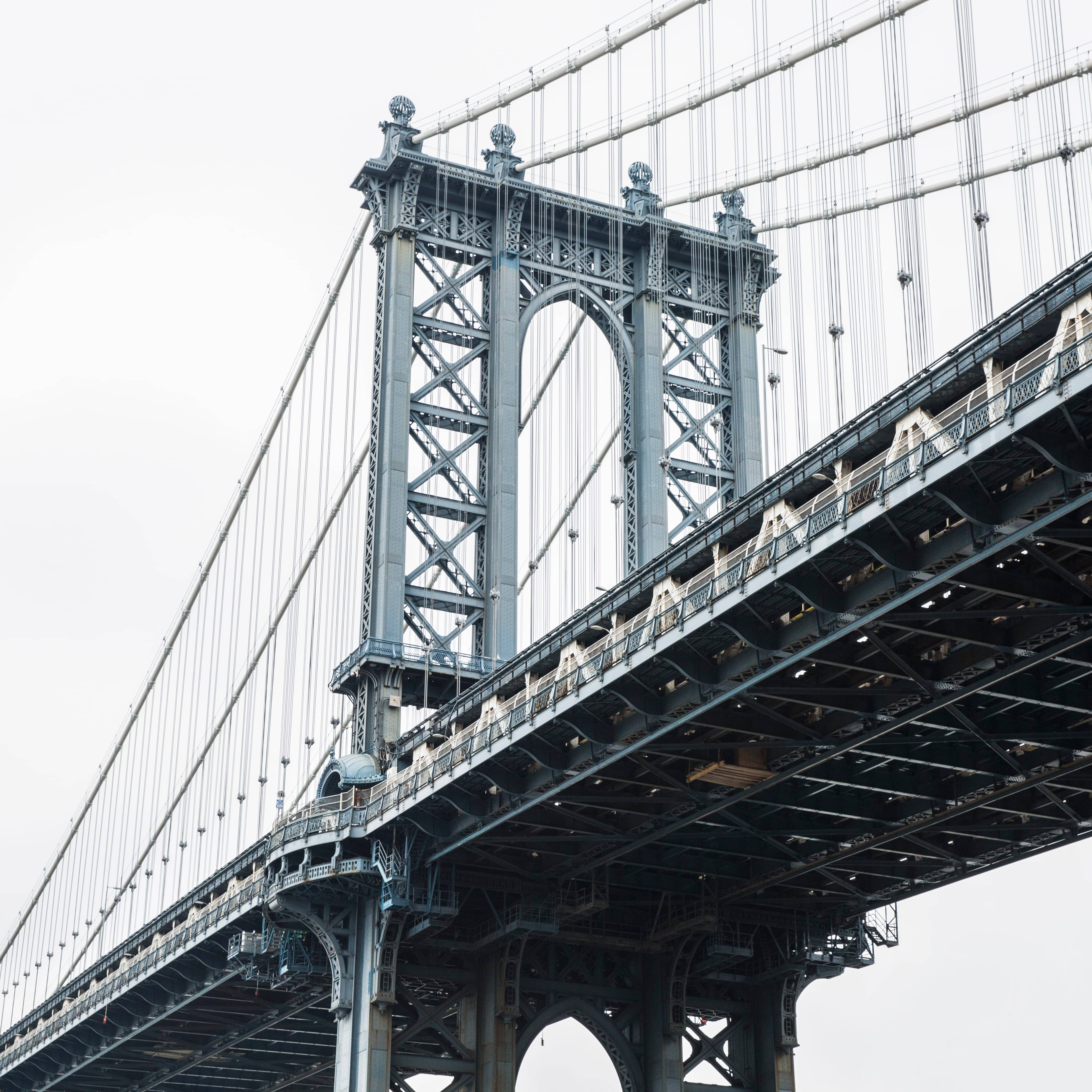 Brooklyn Bridge 桌布 壁紙 — 以低角度觀看曼哈頓大橋的鋼結構，映襯著蒼白的天空，展現複雜的懸索和華麗的塔樓。