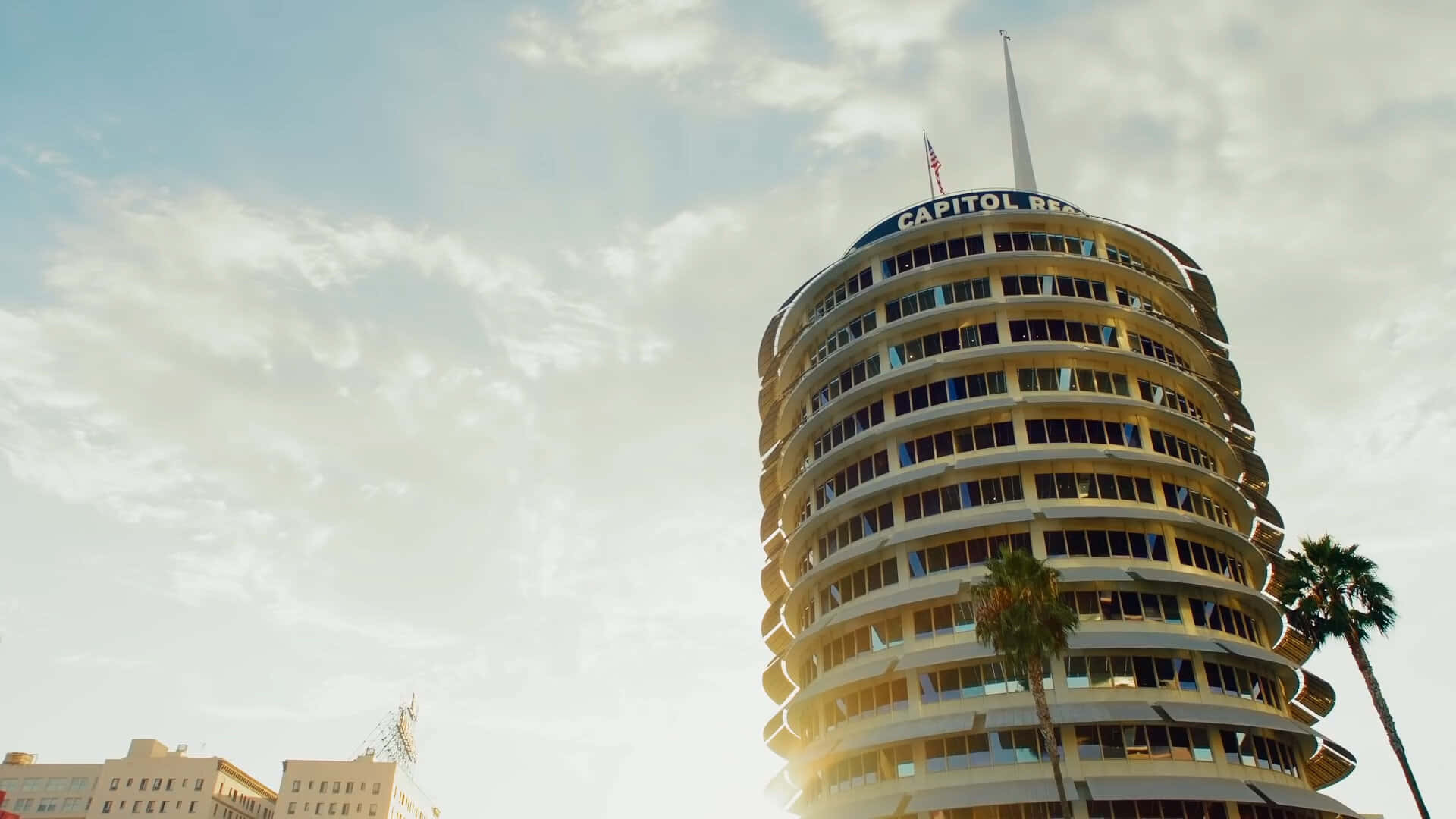Sunny Day 桌布 壁紙 — 以低角度觀看標誌性的 Capitol Records 大樓，沐浴在金色夕陽中，棕櫚樹環繞其螺旋結構。