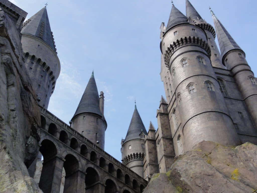 Hogwarts Castle 桌布 壁紙 — 以低角度觀看霍格華茲城堡，其標誌性的石塔和角樓映襯在清澈的藍天下。