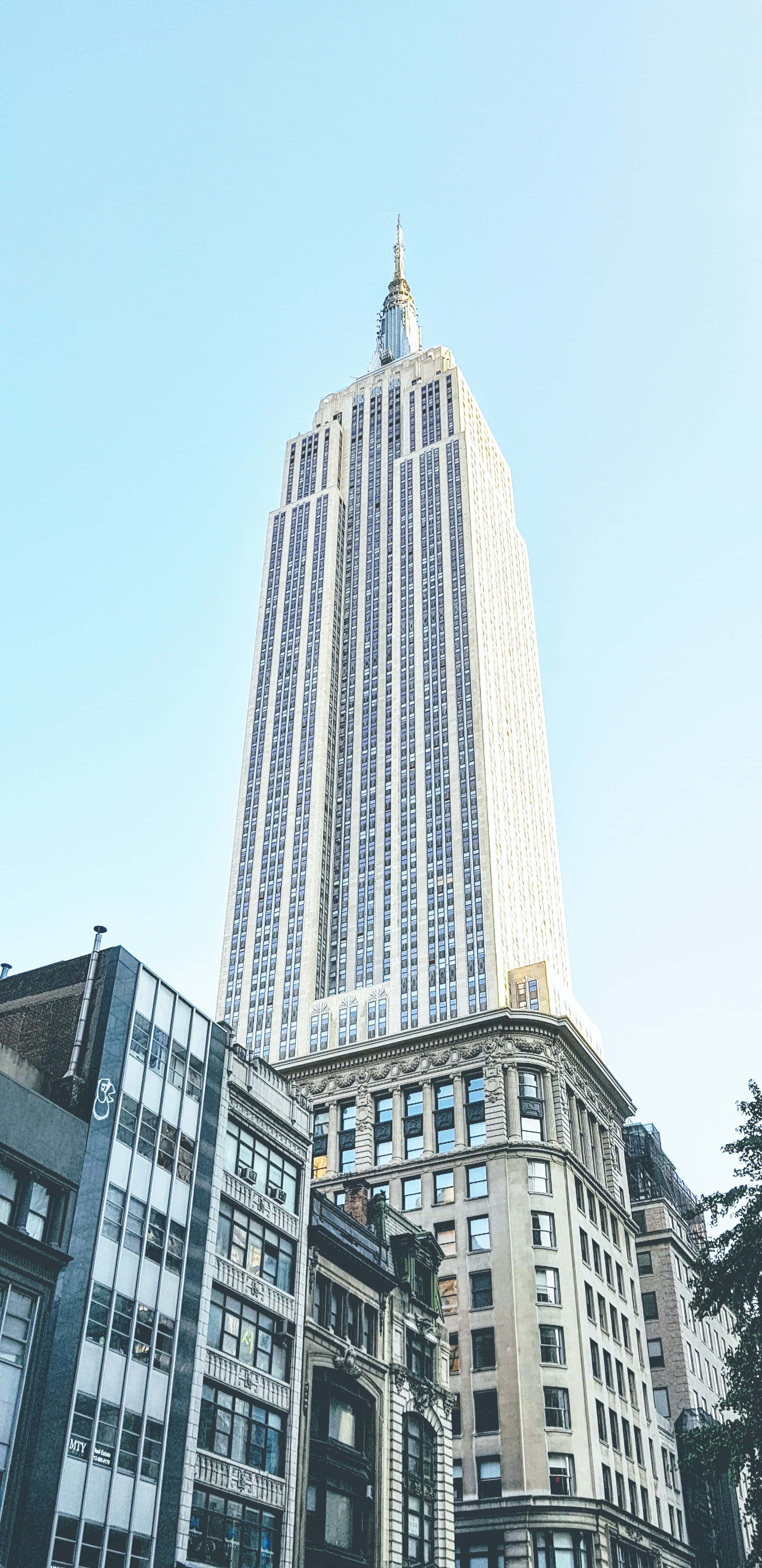 Empire State Building 桌布 壁紙 — 以低角度觀賞帝國大廈刺穿周圍城市建築上方的清澈藍天。