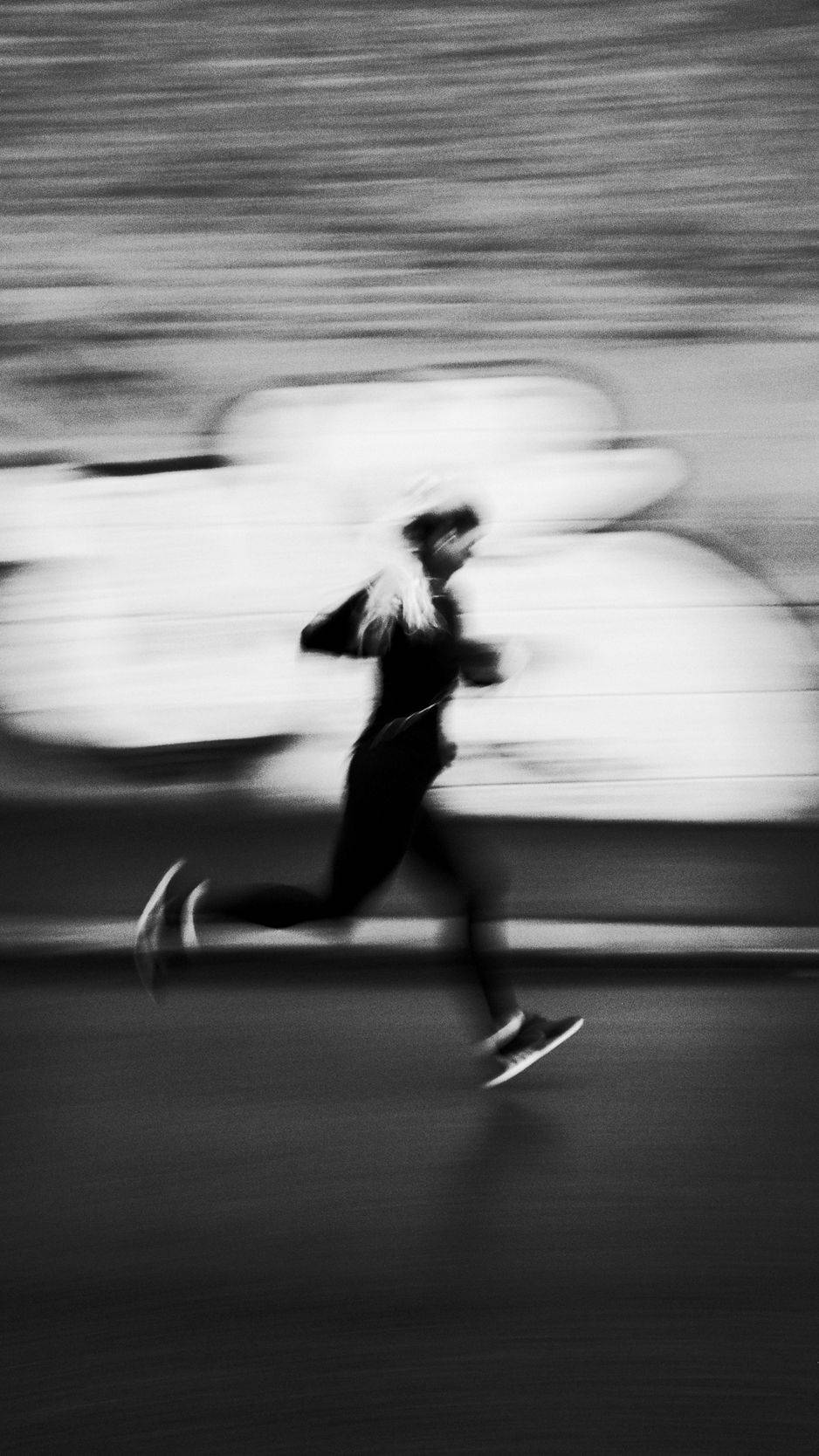 運動 桌布 壁紙 — 以單色調捕捉的跑步者，在有條紋的城市背景下呈現戲劇性的動態模糊效果。