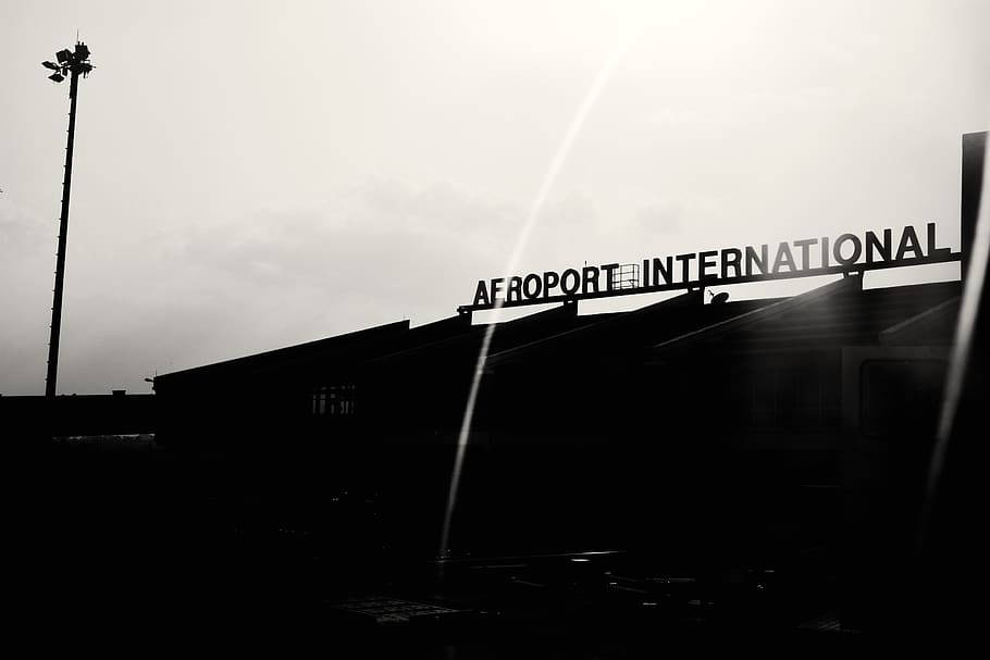 黑白 桌布 壁紙 — 以多雲天空和鏡頭光暈為背景的剪影機場航廈，帶有「AEROPORT INTERNATIONAL」標誌。