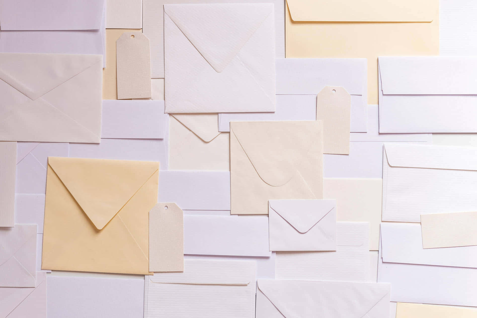 mail 桌布 壁紙 — 以柔和粉彩色調排列的各種奶油色和白色信封及標籤的平鋪佈局。