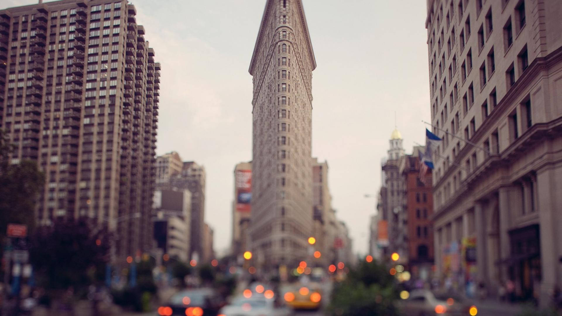 Flatiron Building 桌布 壁紙 — 以標誌性的熨斗大廈為中心，帶有交通散景燈光的模糊城市街景。