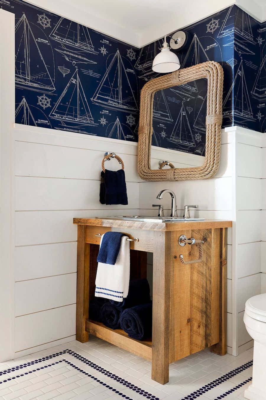 Bathroom Decor 桌布 壁紙 — 以海軍藍帆船藍圖壁紙、白色護牆板牆壁、質樸木製洗手台和繩框鏡子為特色的航海主題浴室。