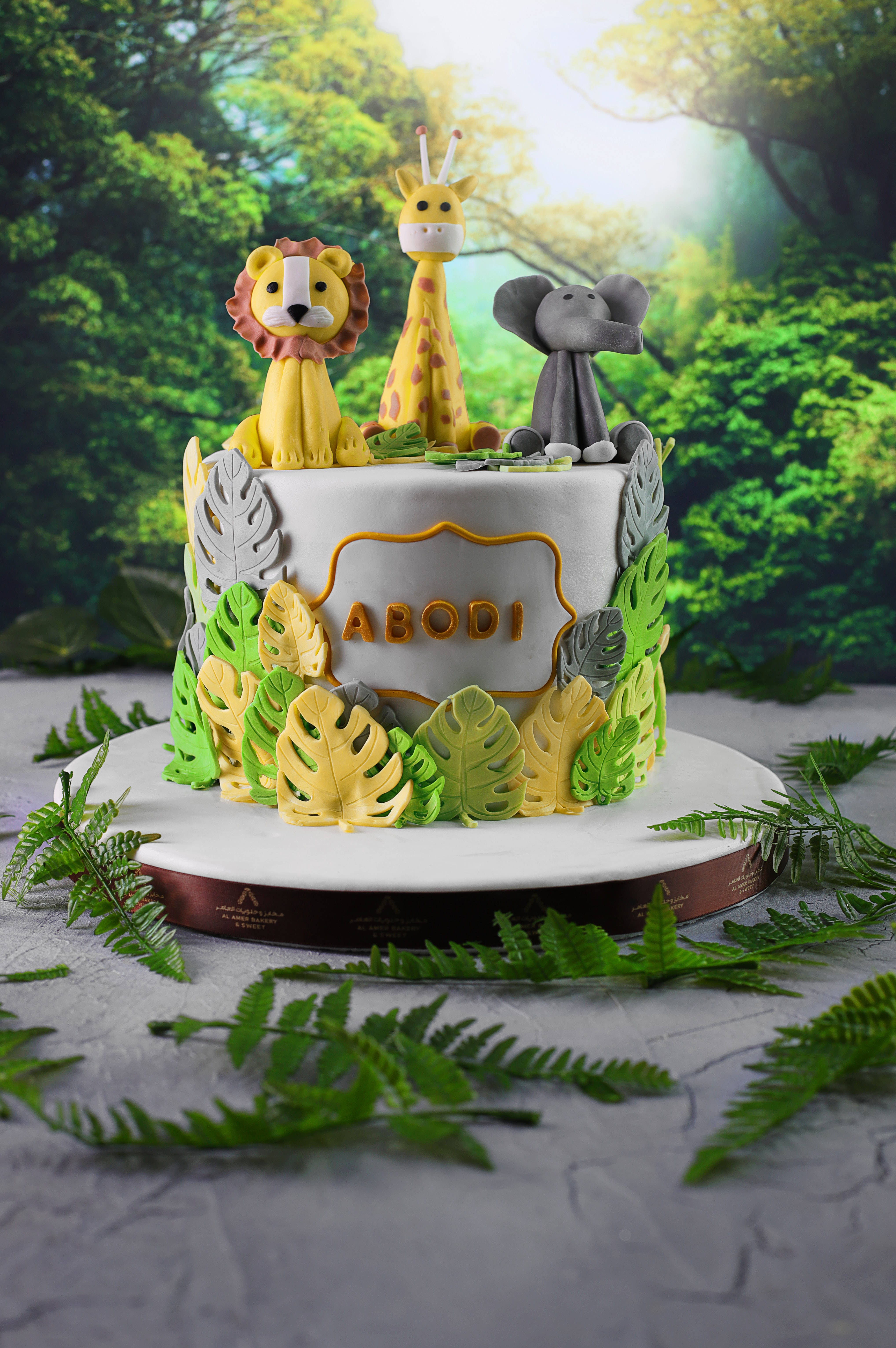 蛋糕 桌布 壁紙 — 以熱帶樹葉環繞的叢林主題生日蛋糕，上面有獅子、長頸鹿和大象公仔。
