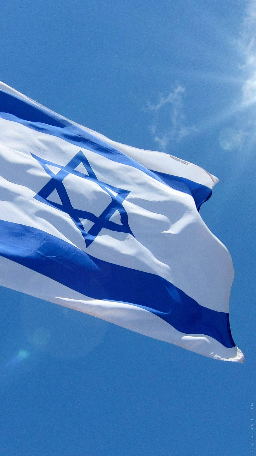 Israel Flag 桌布 壁紙 — 以色列國旗在晴朗藍天、太陽耀斑和縷縷白雲中動態飄揚。