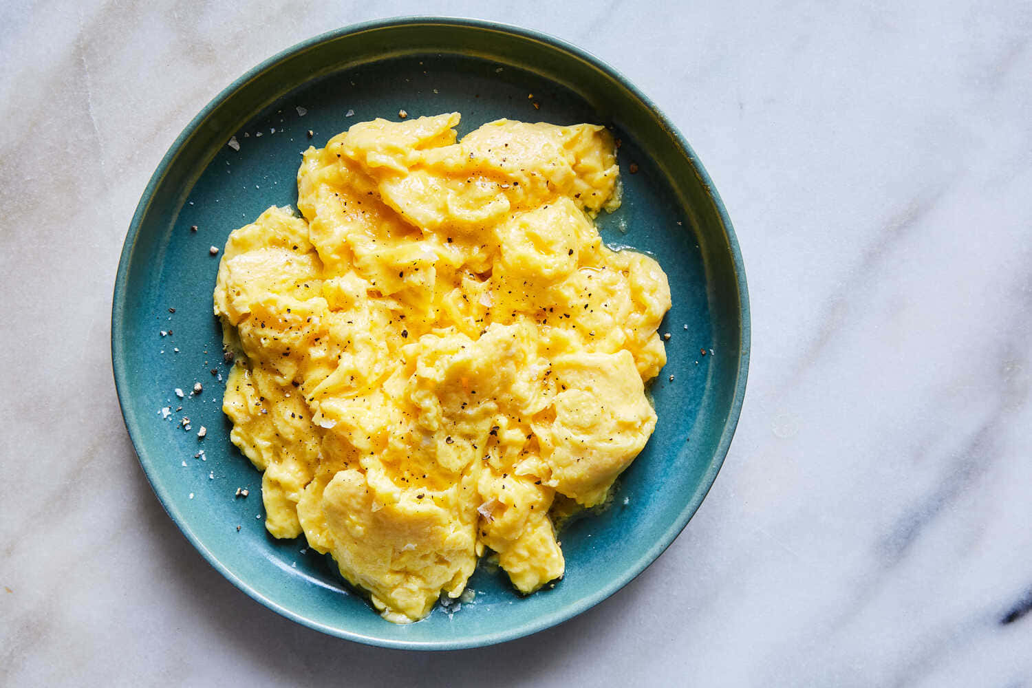Scrambled Egg 桌布 壁紙 — 以鹽和胡椒調味的蓬鬆炒蛋放在白色大理石表面的青綠色盤子上。