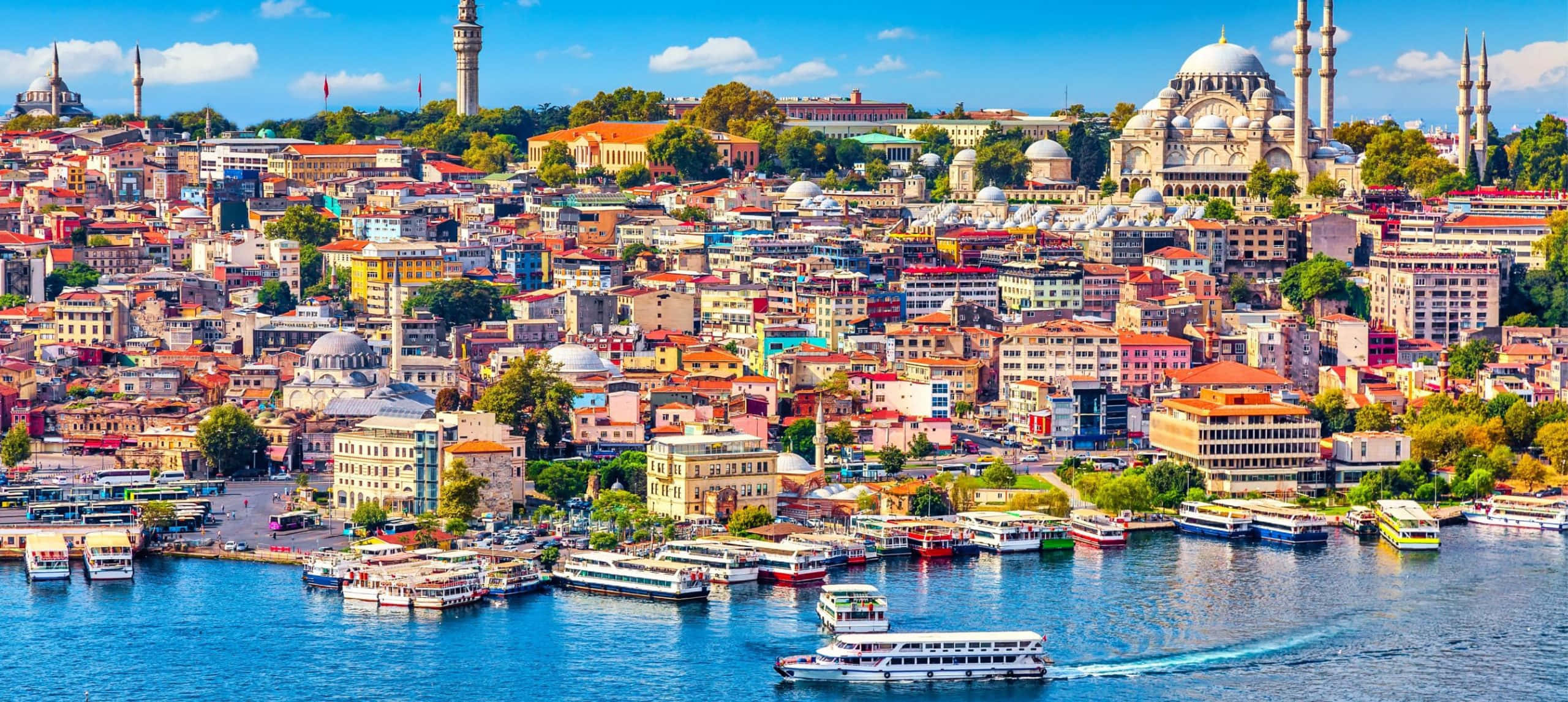 土耳其 桌布 壁紙 — 伊斯坦堡歷史海濱的鳥瞰圖，色彩繽紛的建築物、清真寺和船隻在藍色水面上，天空明亮。