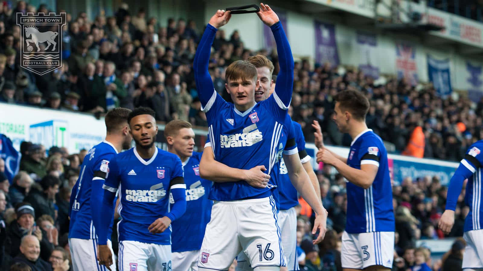 Ipswich Town 桌布 壁紙 — 伊普斯維奇足球員在擠滿觀眾的球場前慶祝進球，身穿藍色球衣。
