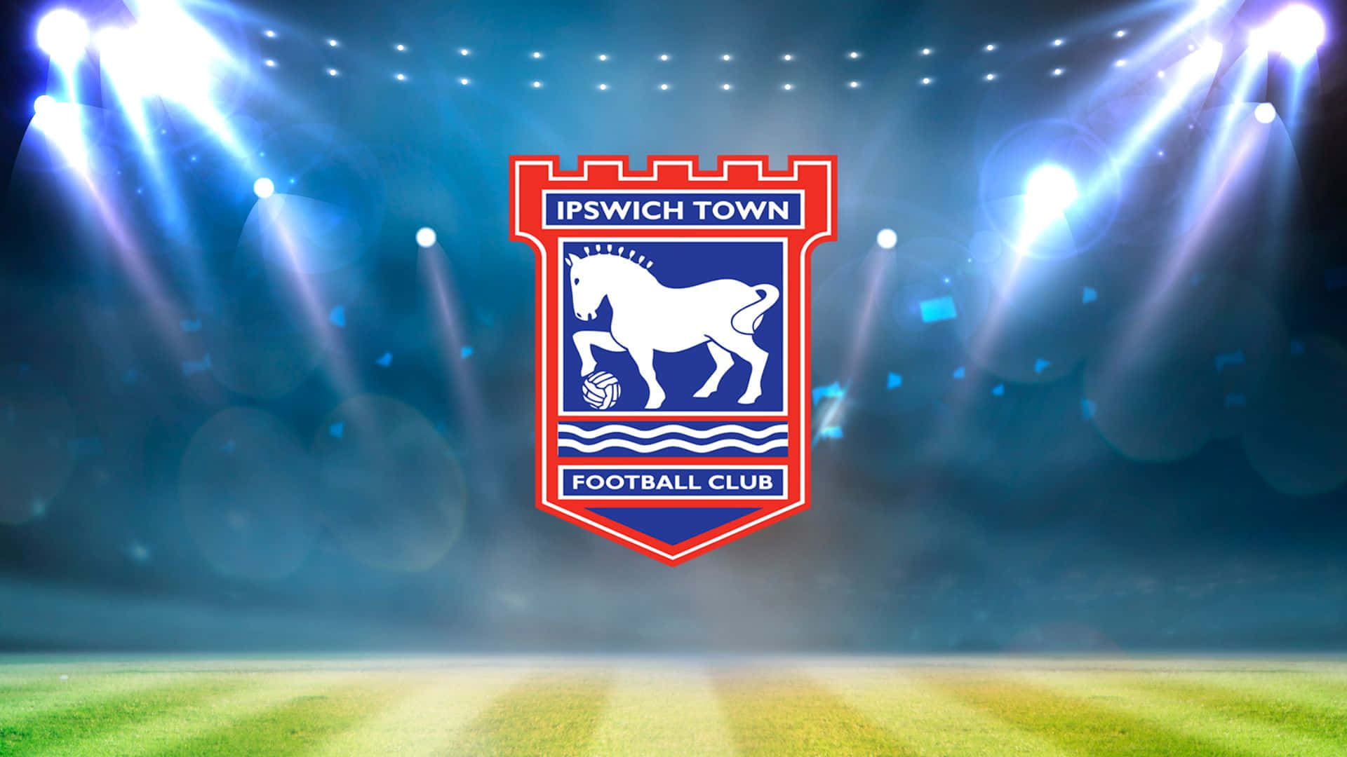 Ipswich Town 桌布 壁紙 — 伊普斯維奇鎮足球俱樂部徽章在充滿活力的綠色球場上被球場聚光燈照亮。