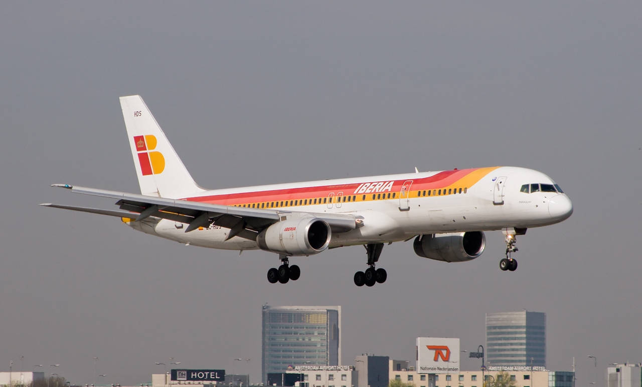 飛機 桌布 壁紙 — 伊比利亞航空白色、紅色和黃色塗裝的飛機放下起落架，在朦朧的城市天際線中下降。