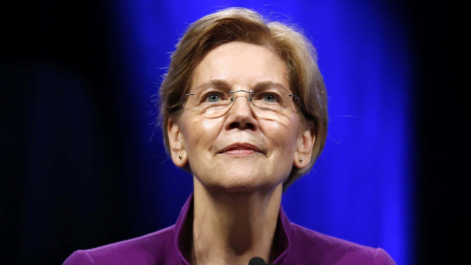 Politics 桌布 壁紙 — 伊莉莎白·華倫的近距離肖像，她抬頭向上看，表情深思，背景是深藍色。