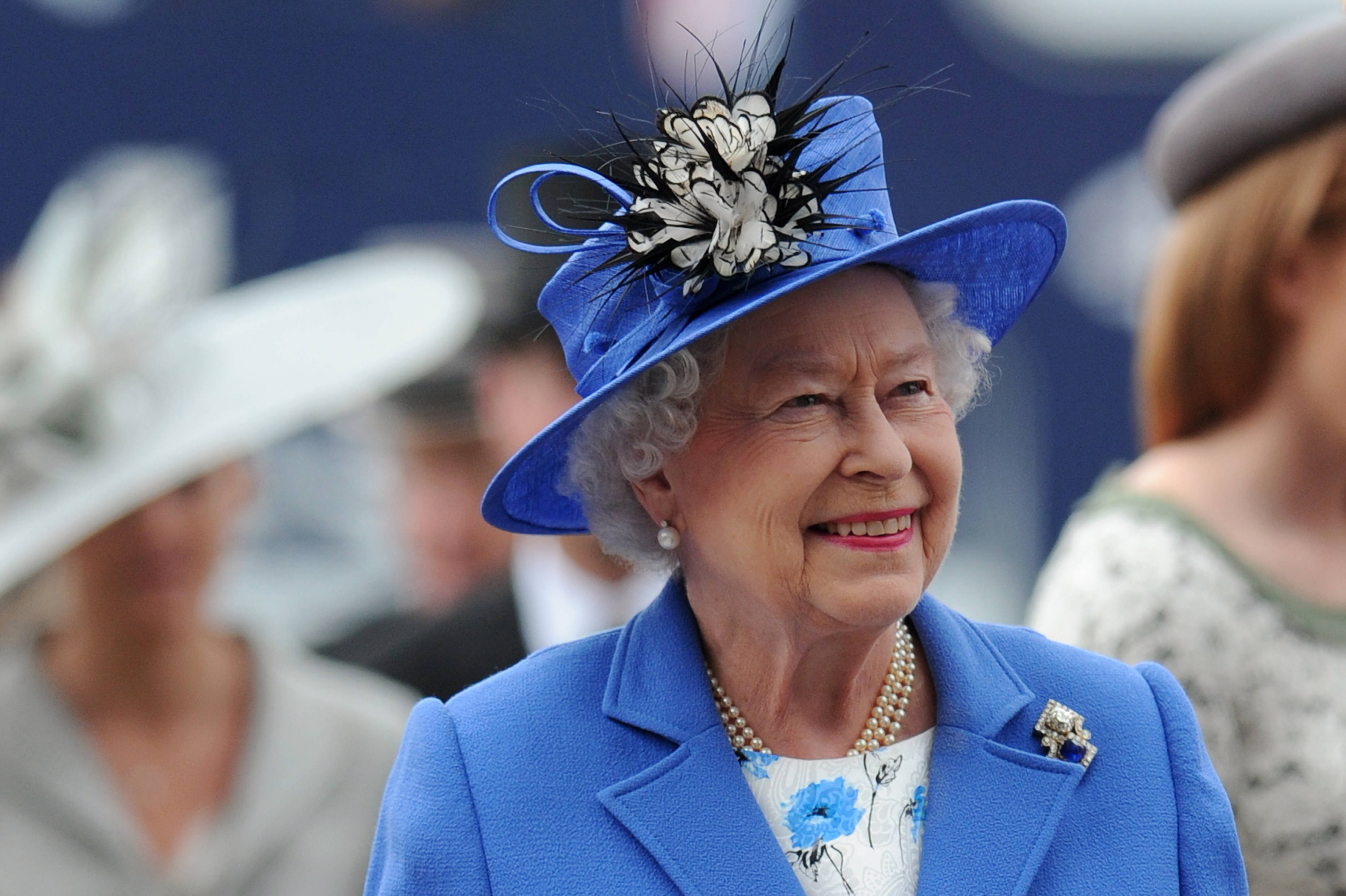 Queen Elizabeth 桌布 壁紙 — 伊莉莎白二世女王在公眾活動中戴著鮮豔的藍色帽子和相配的外套，溫暖地微笑。
