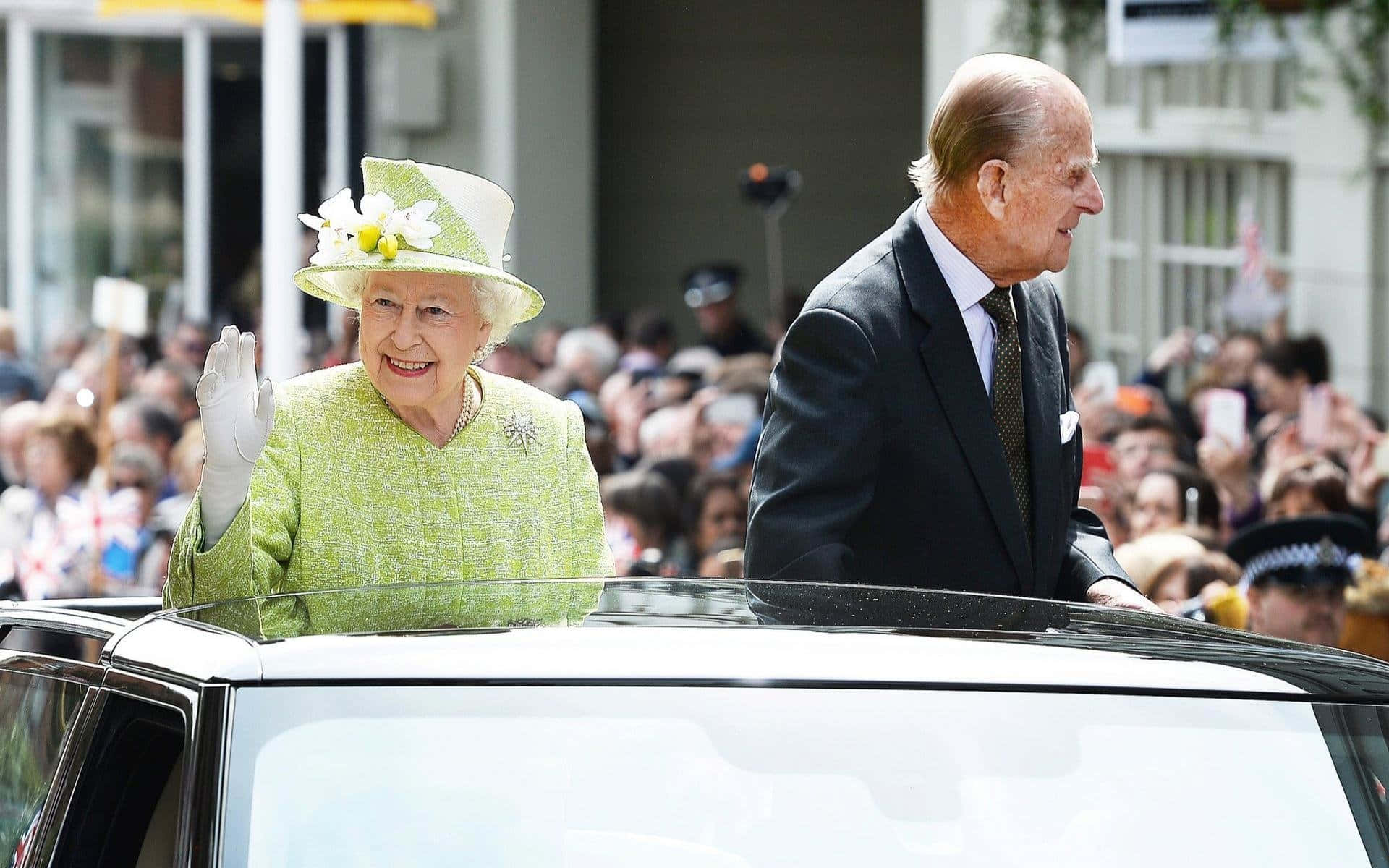 Queen Elizabeth 桌布 壁紙 — 伊莉莎白二世女王在公眾遊行期間從車窗愉快地揮手，菲利普親王站在她身旁。