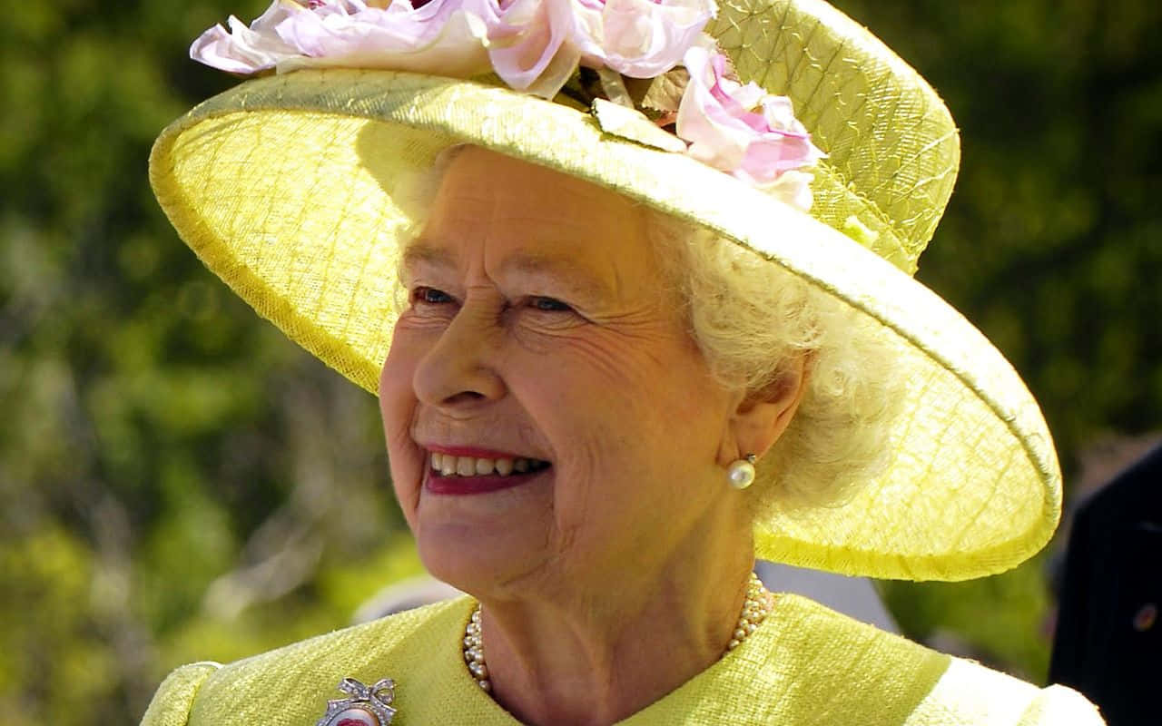 Queen Elizabeth 桌布 壁紙 — 伊莉莎白二世女王戴著一頂飾有粉紅色花朵的亮黃色帽子，在陽光普照的綠色背景下溫暖地微笑。
