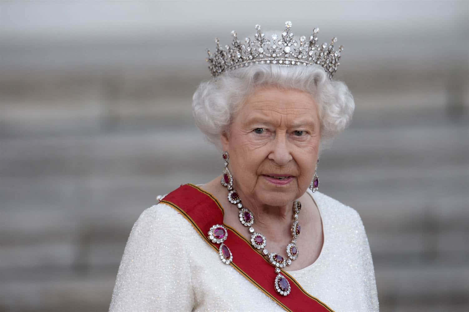 Queen Elizabeth 桌布 壁紙 — 伊莉莎白二世女王戴著閃閃發光的鑽石头饰和紅寶石飾帶，背景是模糊的石牆。