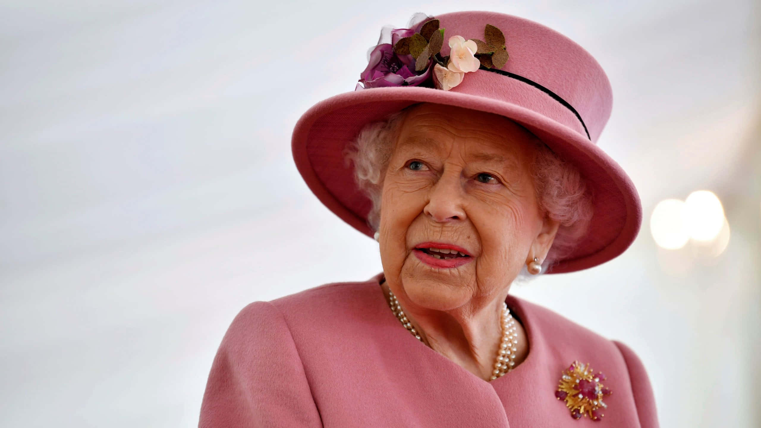 Queen Elizabeth 桌布 壁紙 — 伊莉莎白二世女王身穿粉紅色外套和飾有花朵的配套帽子，以溫柔的表情向上仰望。
