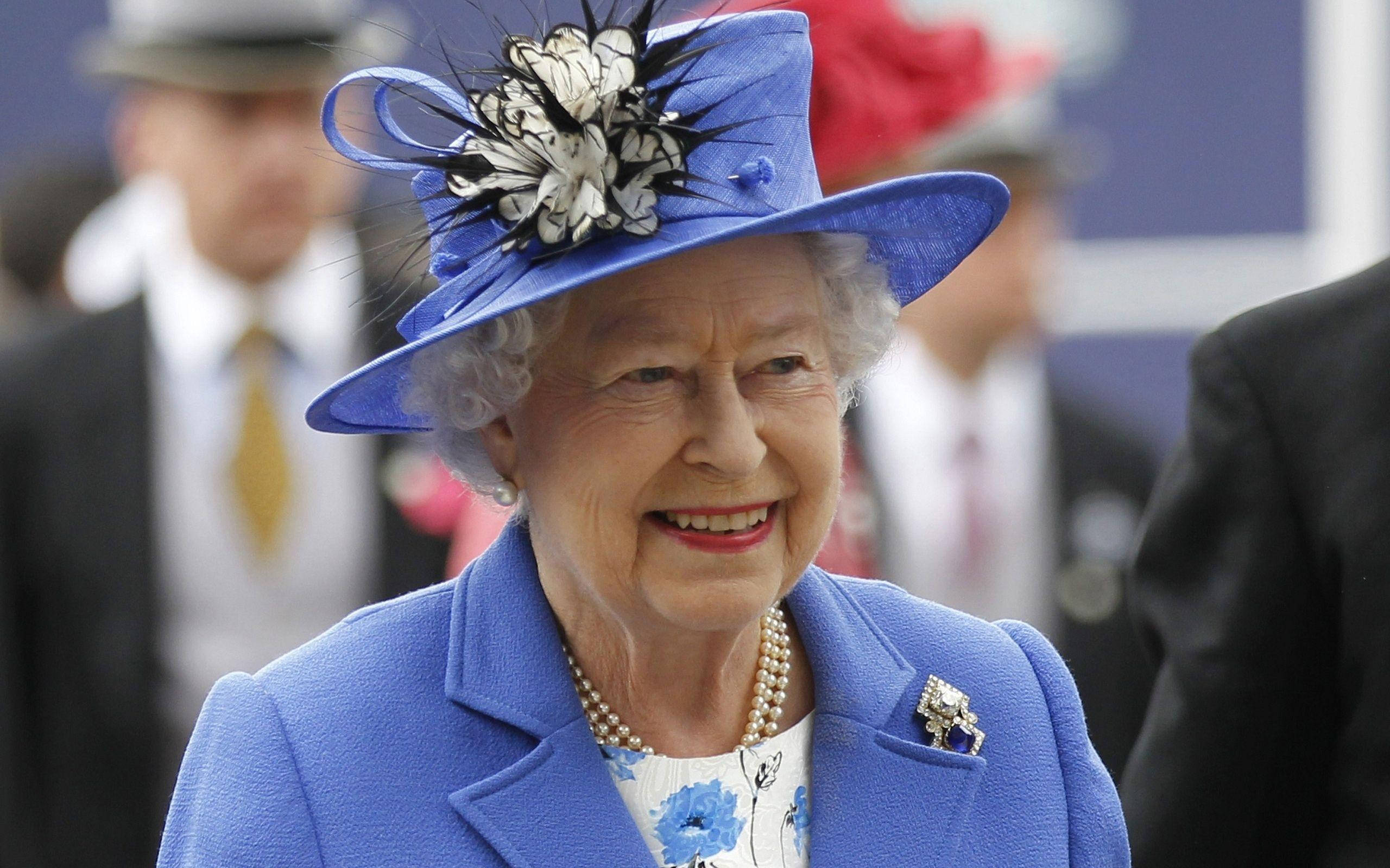 Queen Elizabeth 桌布 壁紙 — 伊莉莎白二世女王身穿鮮藍色外套和搭配的帽子，帽上飾有黑白羽毛，露出溫暖的笑容。
