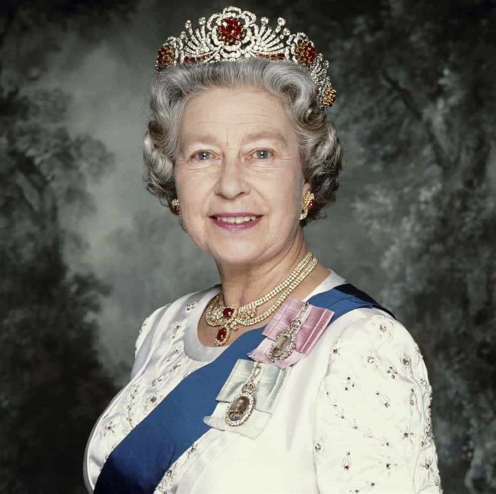 Queen Elizabeth 桌布 壁紙 — 伊莉莎白二世女王面帶微笑，威嚴地佩戴著鑲有珠寶的王冠、珍珠項鍊和藍色肩帶，背景是柔和的森林。