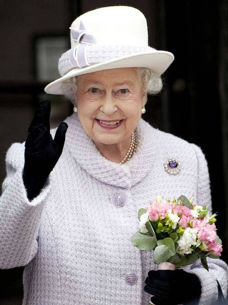 Queen Elizabeth 桌布 壁紙 — 伊莉莎白二世女王面帶溫暖微笑，揮手並手持一束粉紅和白色鮮花，身穿淺薰衣草色外套和白色帽子。