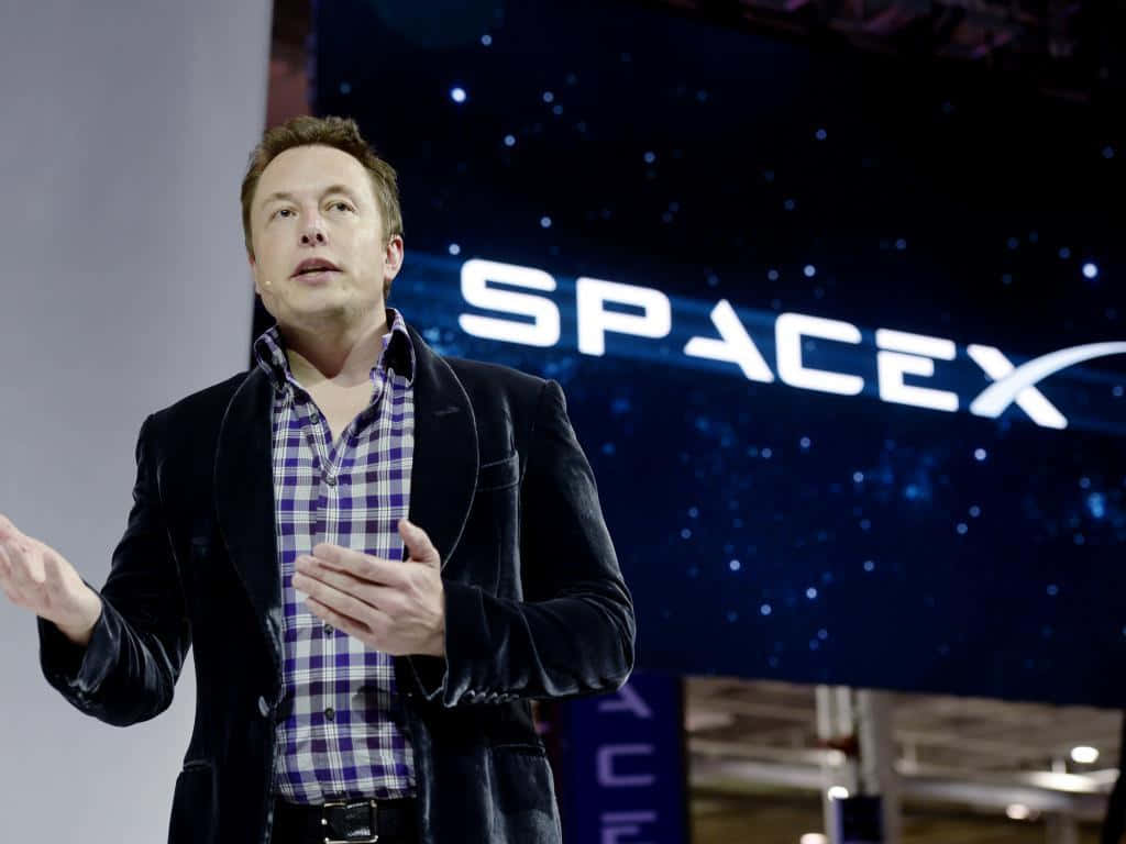 伊隆·馬斯克 桌布 壁紙 — 伊隆·馬斯克在星空背景下於 SpaceX 活動中熱情地比劃手勢發言。