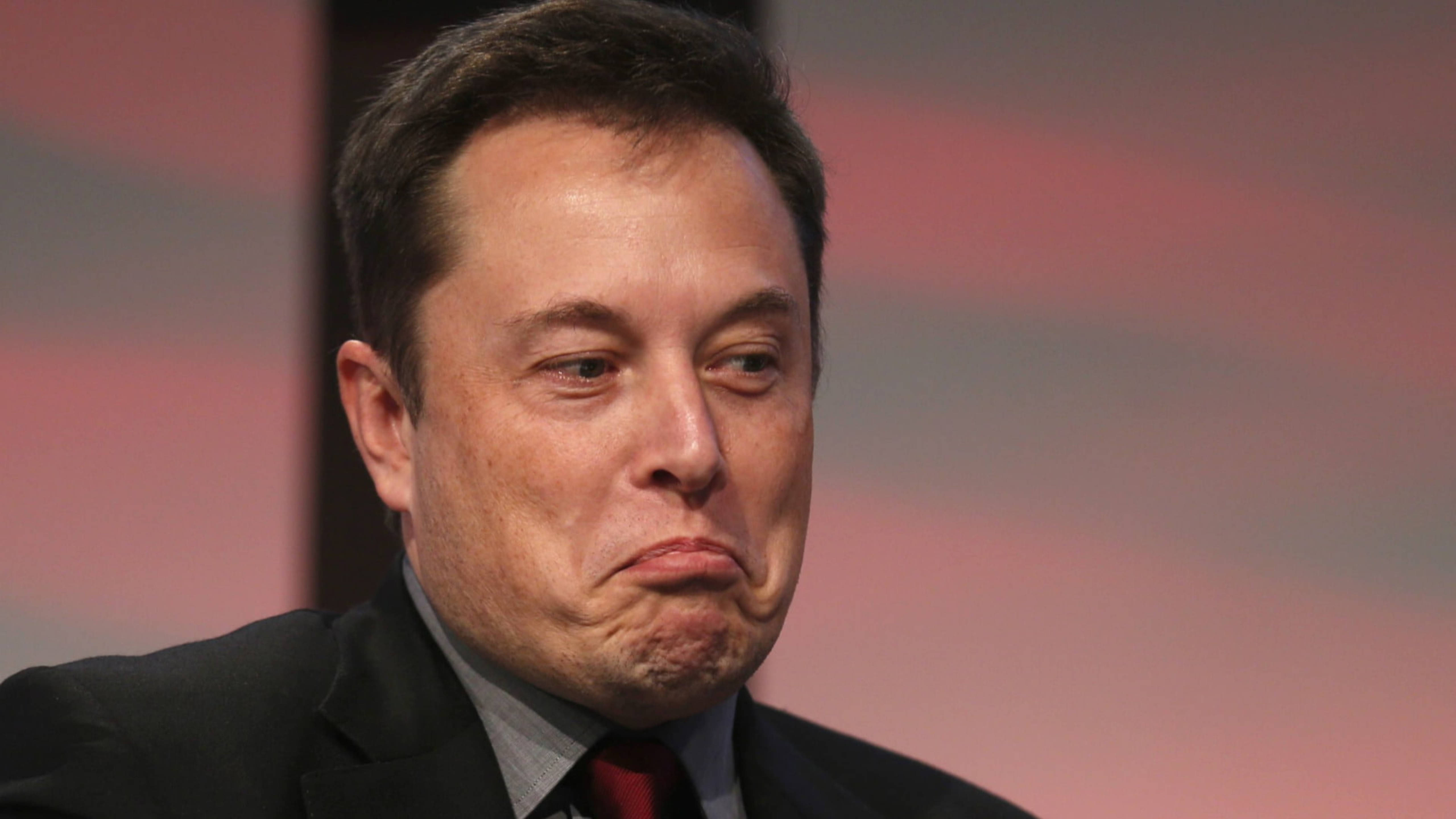 Elon 桌布 壁紙 — 伊隆·馬斯克的特寫，他穿著深色西裝和紅色領帶，在模糊的粉紅色背景前做出噘嘴表情。