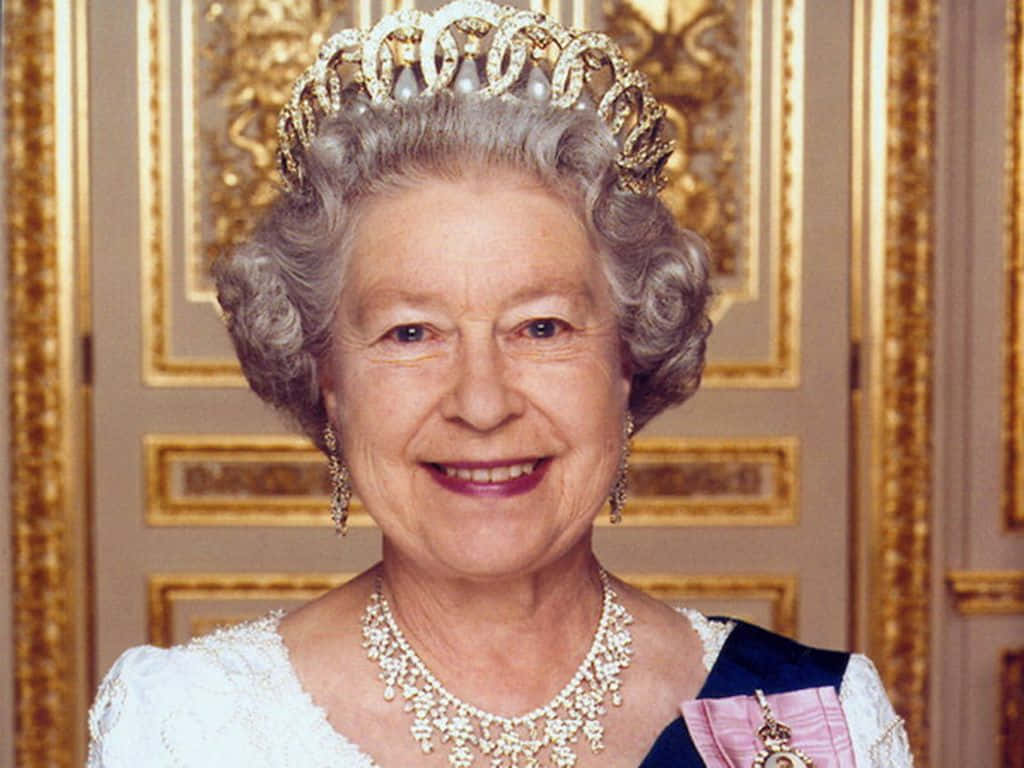 Queen Elizabeth 桌布 壁紙 — 伊麗莎白二世女王戴著鑲有寶石的王冠和珍珠項鍊，在金色華麗的門背景下溫暖地微笑。