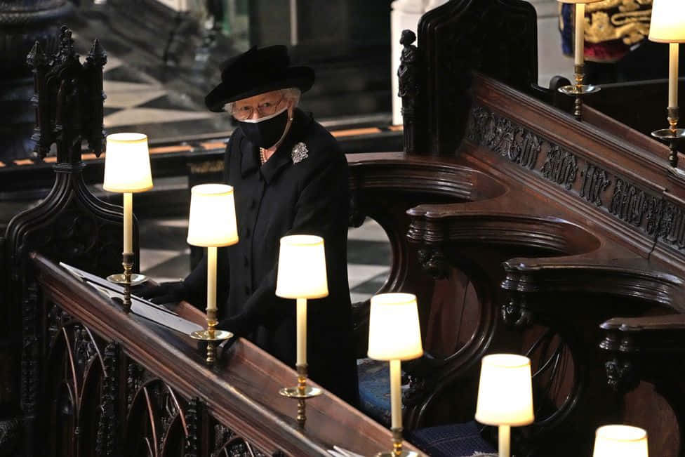 Funeral 桌布 壁紙 — 伊麗莎白二世女王身穿黑色外套和帽子，莊嚴地站在宏偉大教堂中由溫暖燭光照亮的華麗木製長椅後面。