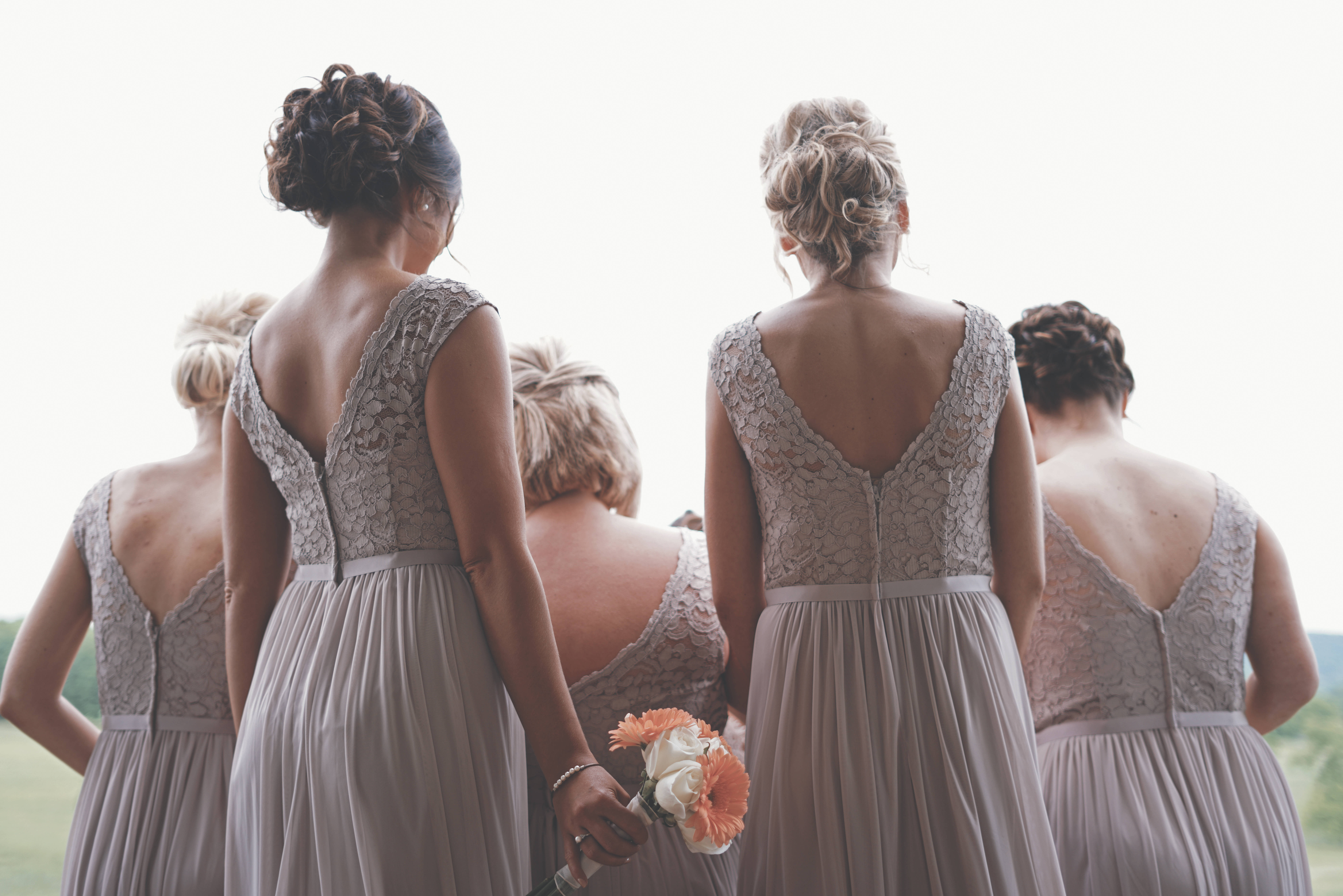 Bridesmaids 桌布 壁紙 — 伴娘們穿著優雅的灰色蕾絲連衣裙，背對鏡頭，手持一束橙色和白色的花束。
