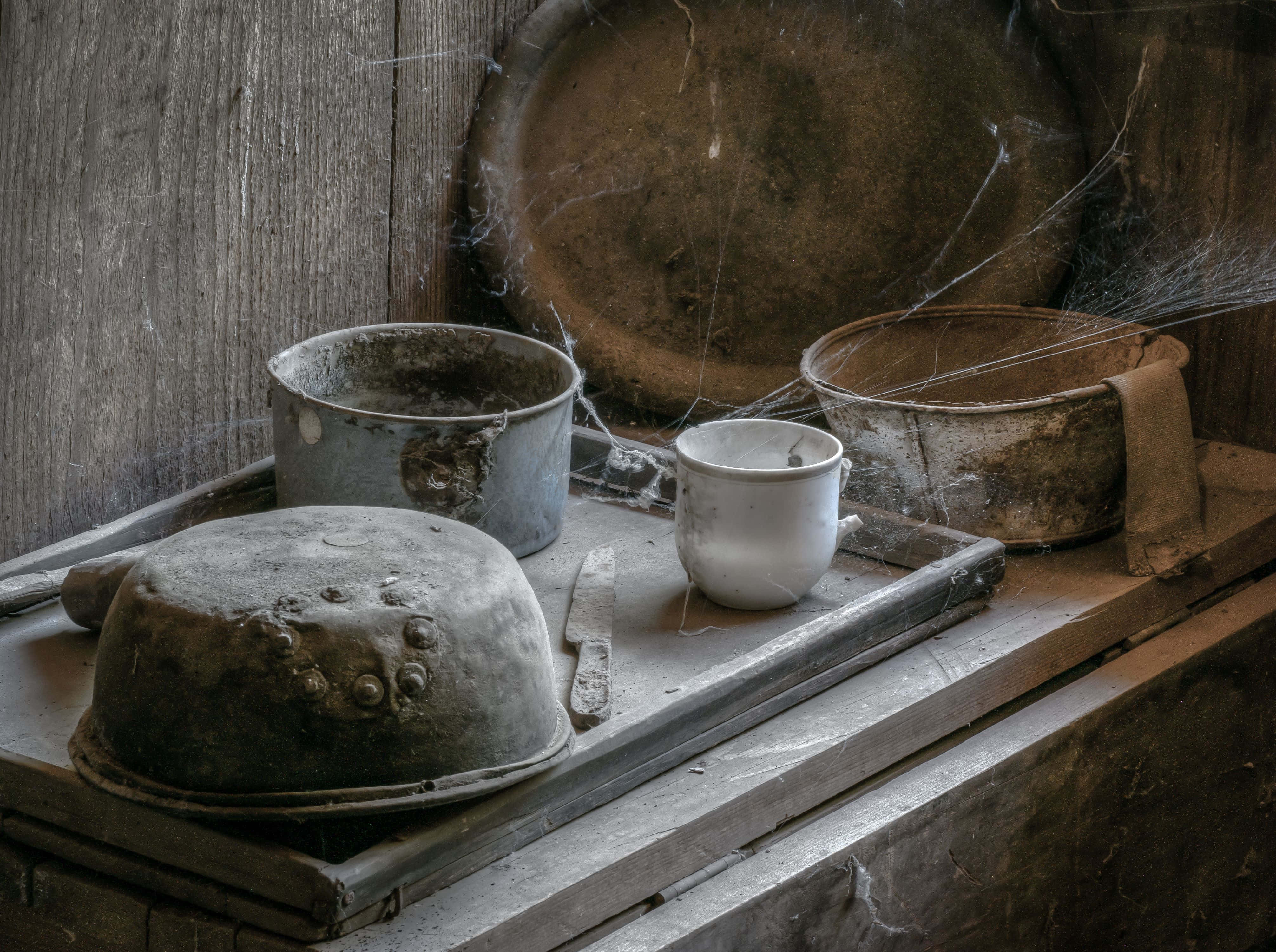 Cobwebs 桌布 壁紙 — 佈滿灰塵的復古廚房用具，包括鍋子和杯子，放在一個佈滿蜘蛛網的木托盤上，背景是風化的木牆。