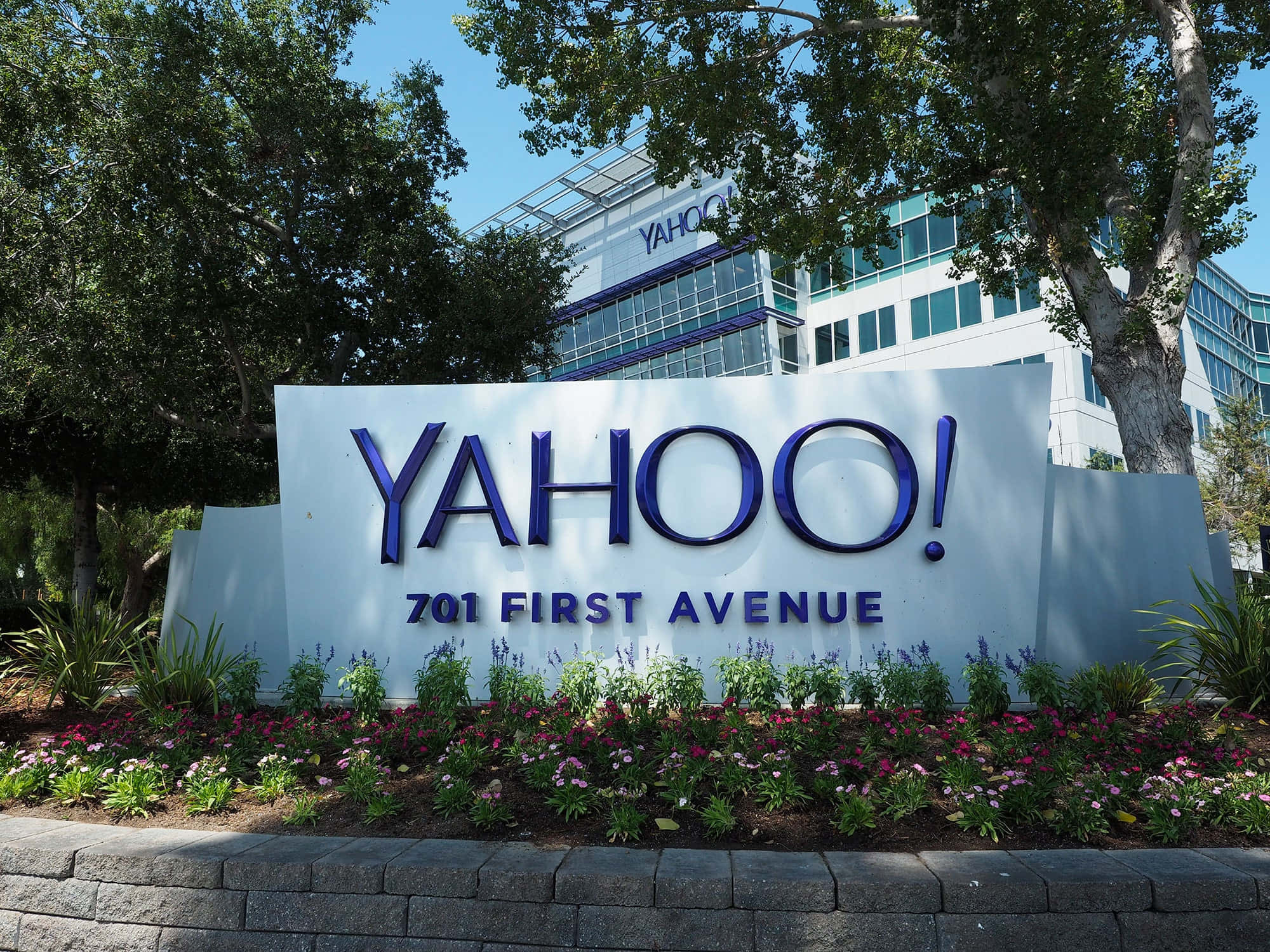 Yahoo 桌布 壁紙 — 位於701 First Avenue的大型藍色Yahoo標誌，被綠樹和色彩繽紛的花朵環繞，在晴朗的藍天下。