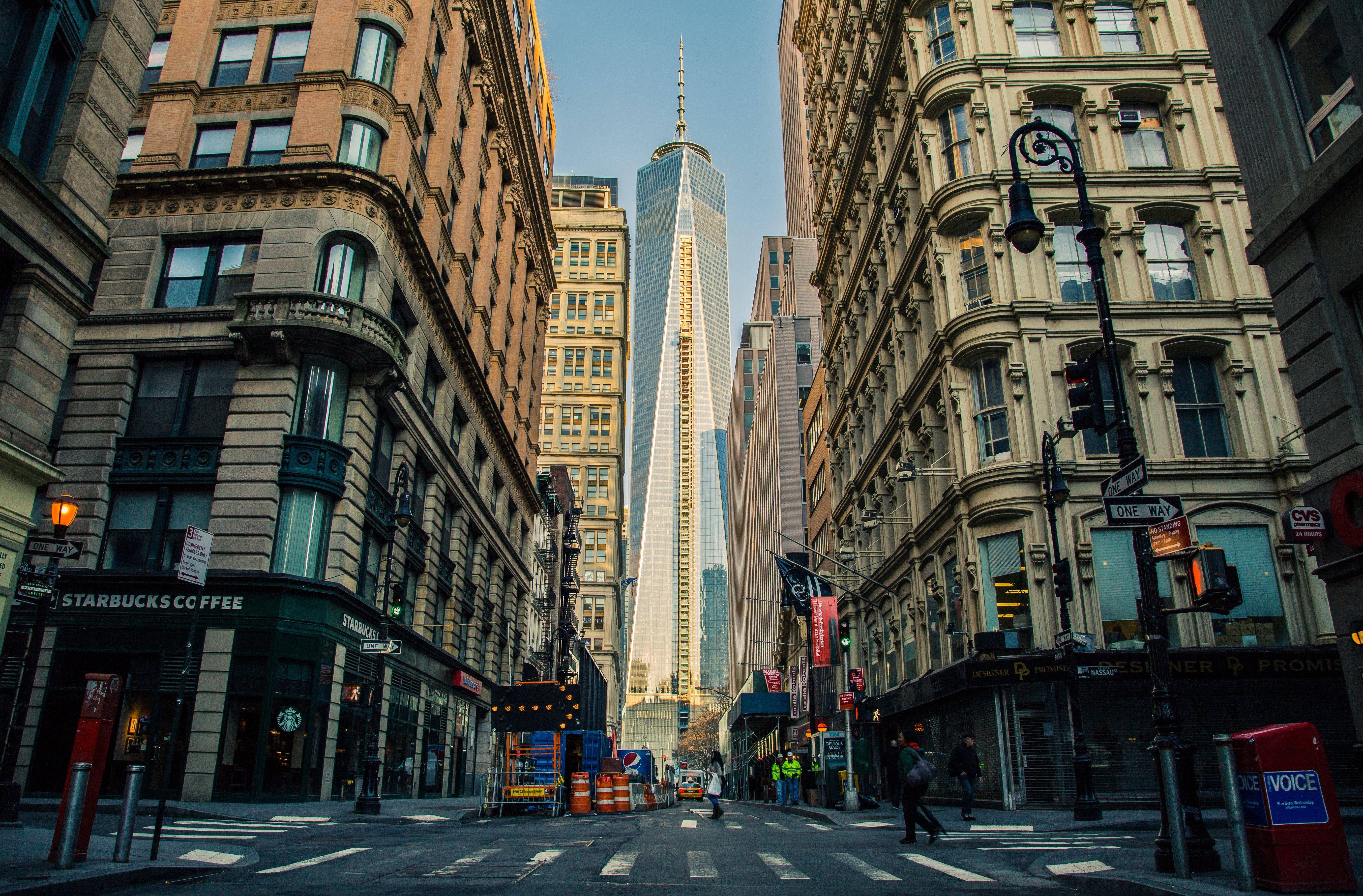 New York 桌布 壁紙 — 低角度城市街景，由歷史建築物框住，自由塔刺穿天空。