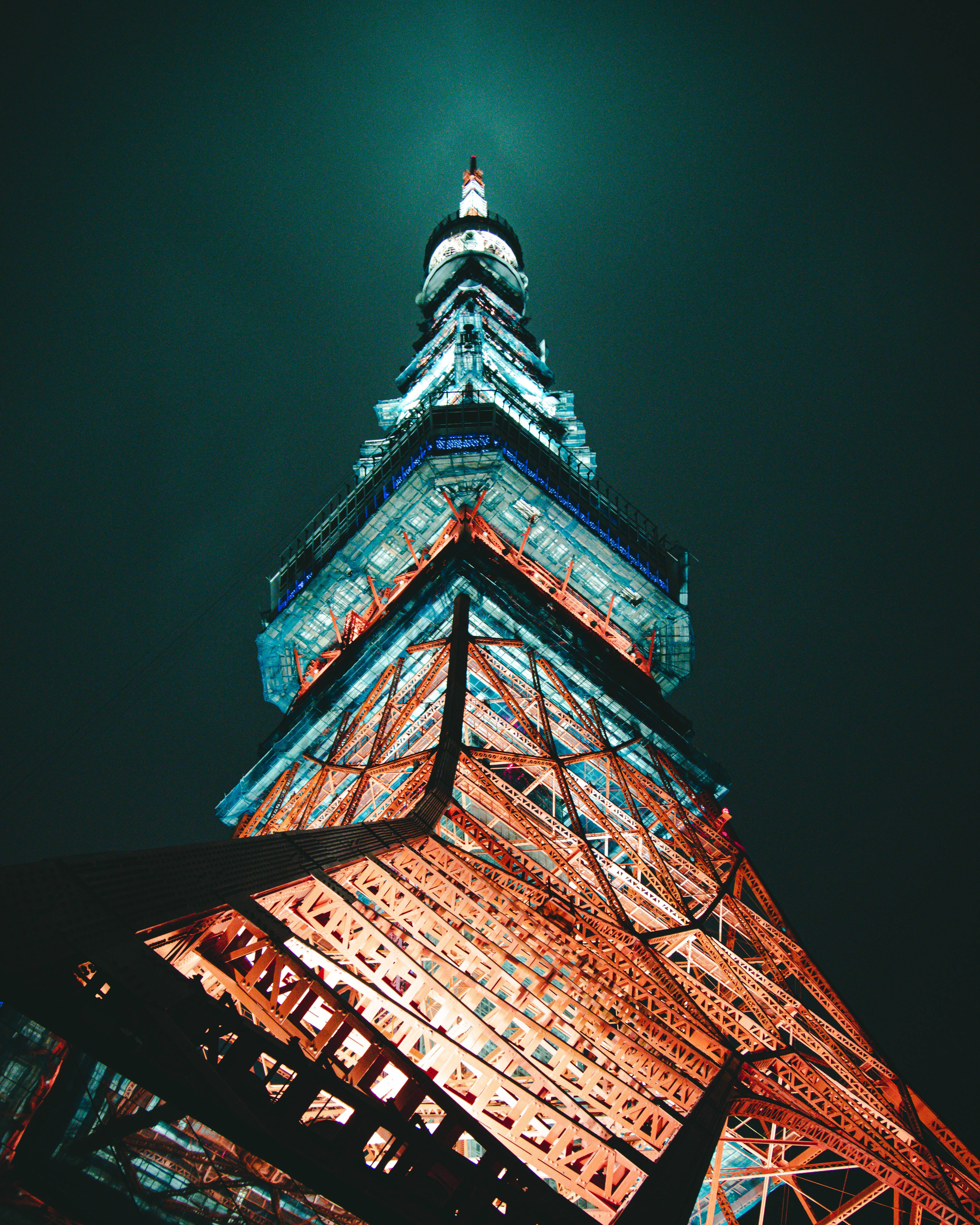 日本 桌布 壁紙 — 低角度夜拍東京鐵塔，溫暖的橙色和冷藍色燈光在深藍綠色天空下閃耀。