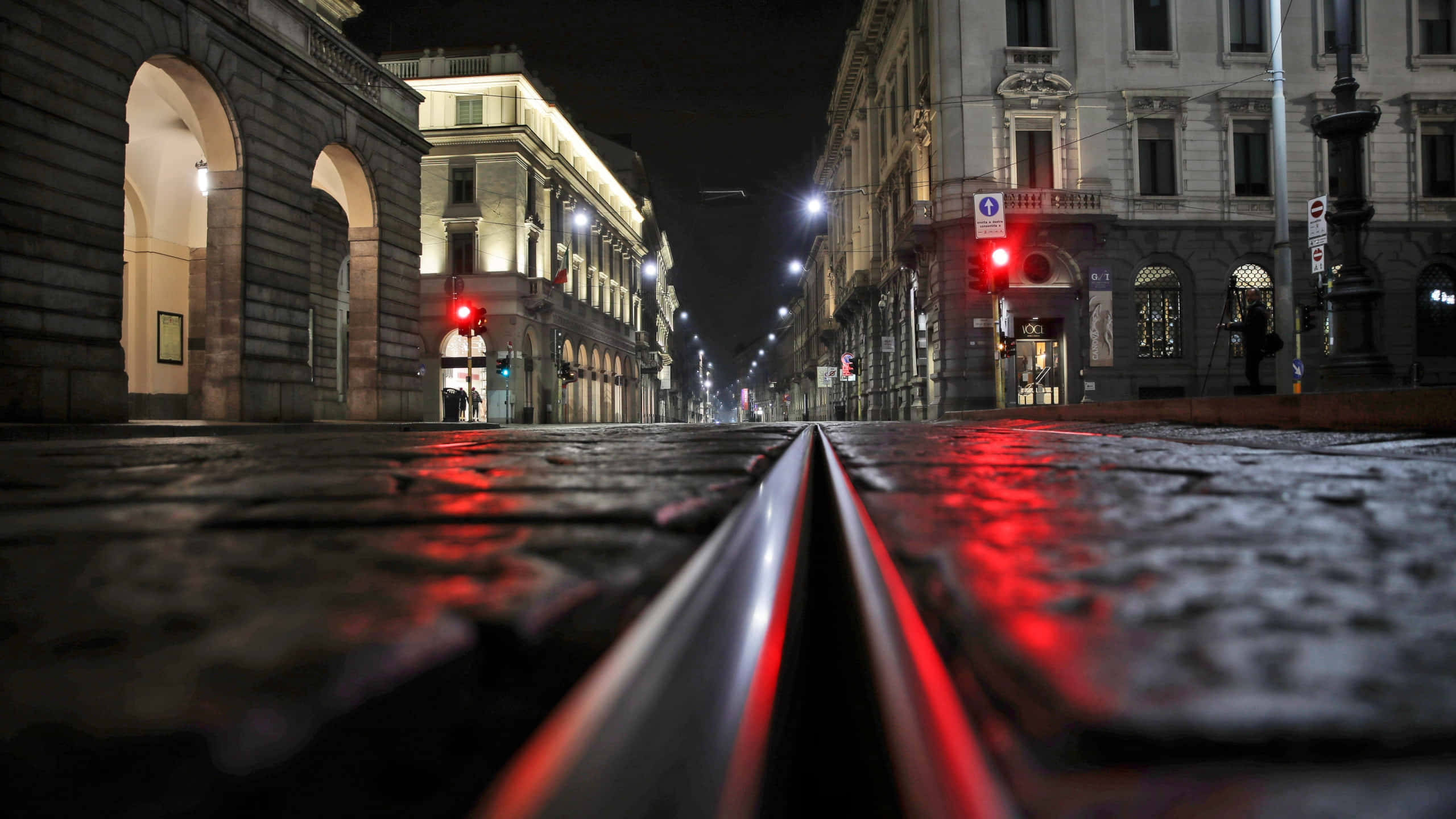 Milan 桌布 壁紙 — 低角度夜攝濕滑鵝卵石街道，電車軌道通向紅色交通燈和歷史建築。