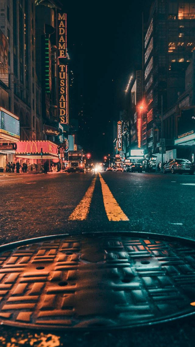 深色 iPhone 桌布 壁紙 — 低角度夜間拍攝濕漉漉的城市街道，前景有發光的霓虹燈招牌和人孔蓋。