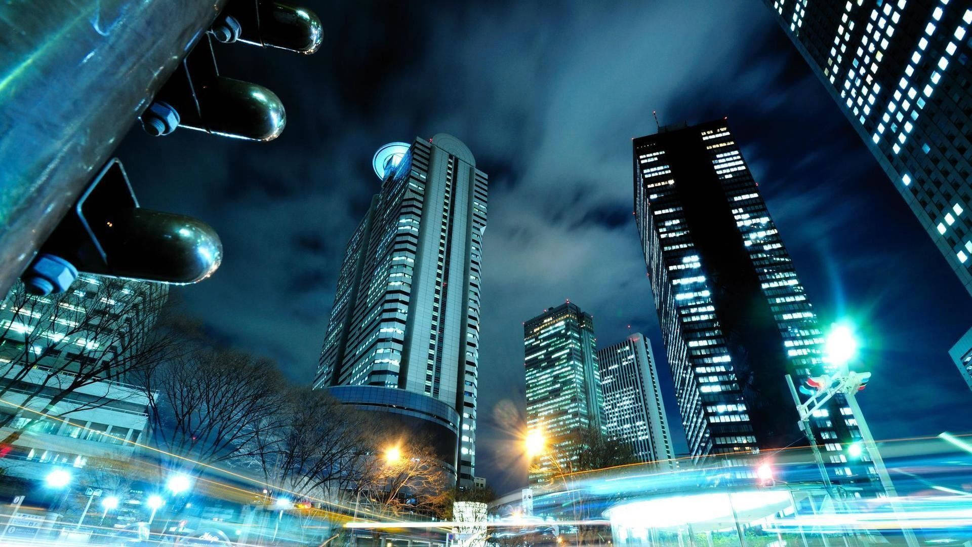 動漫城市 桌布 壁紙 — 低角度夜間拍攝高聳摩天大樓，車流光軌在陰天天空下劃過。