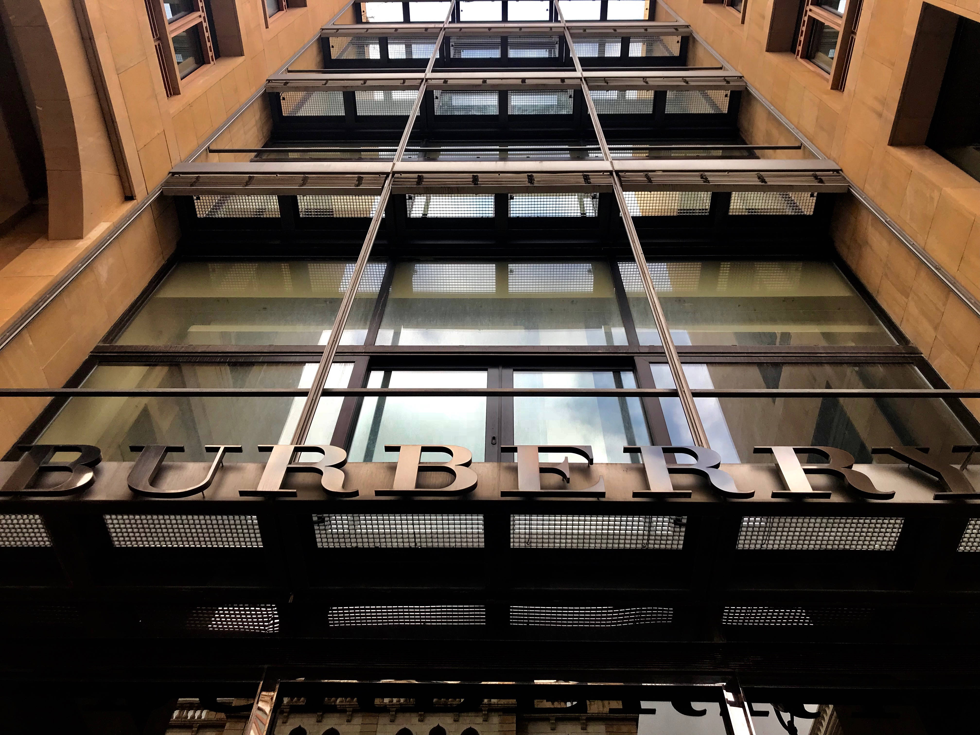 Burberry 桌布 壁紙 — 低角度拍攝 Burberry 商店的玻璃和鋼結構外牆，在溫暖的石牆上帶有粗體金屬字體。