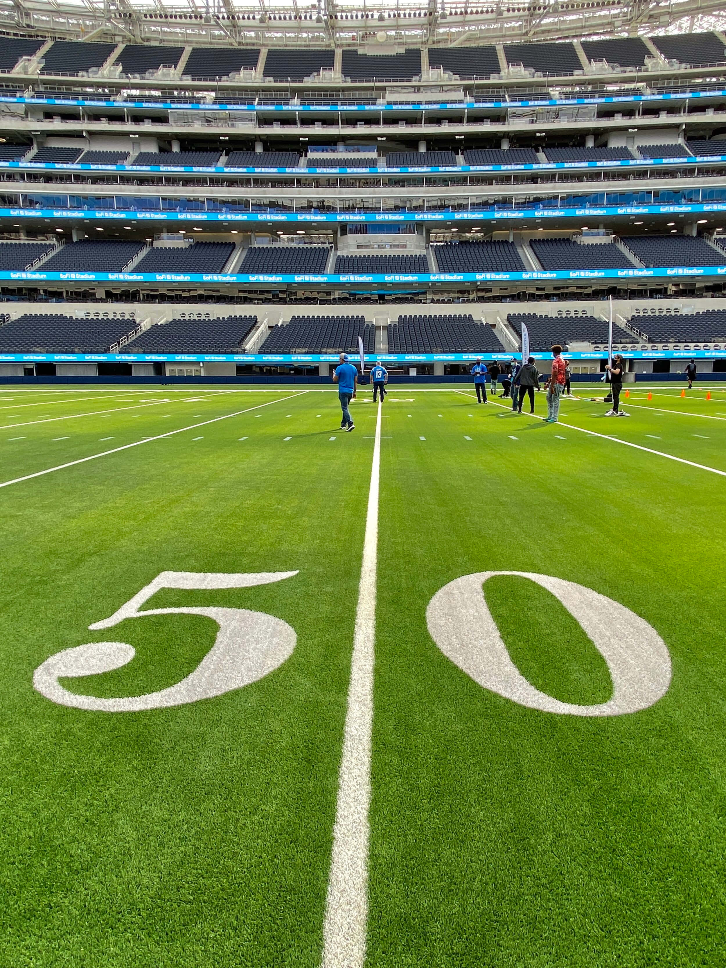 Sofi Stadium 桌布 壁紙 — 低角度拍攝一個充滿活力的綠色足球場，上面有白色塗漆的50號，周圍是空無一人的體育場座位，在明亮的日光下。