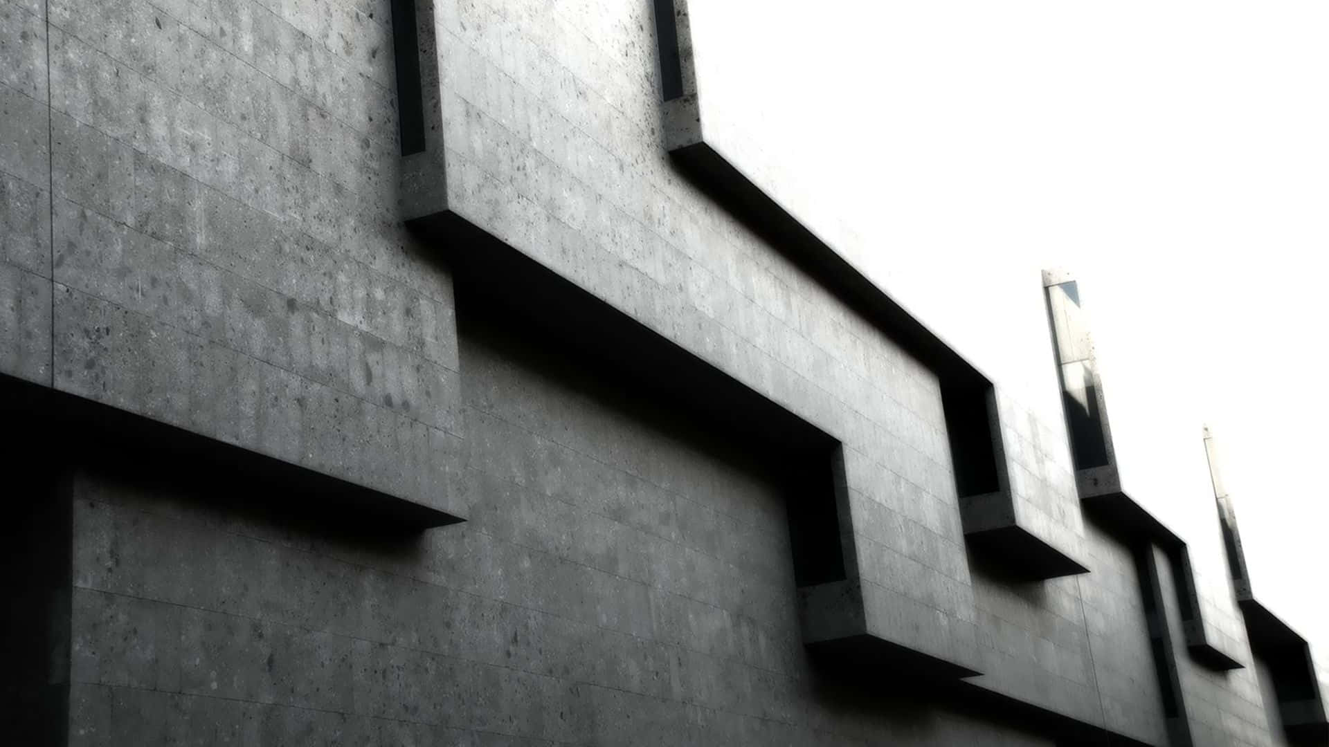 Black And White Architecture 桌布 壁紙 — 低角度拍攝一座樸素的粗獷主義混凝土建築，帶有鮮明的幾何突出物，映襯著明亮的天空。