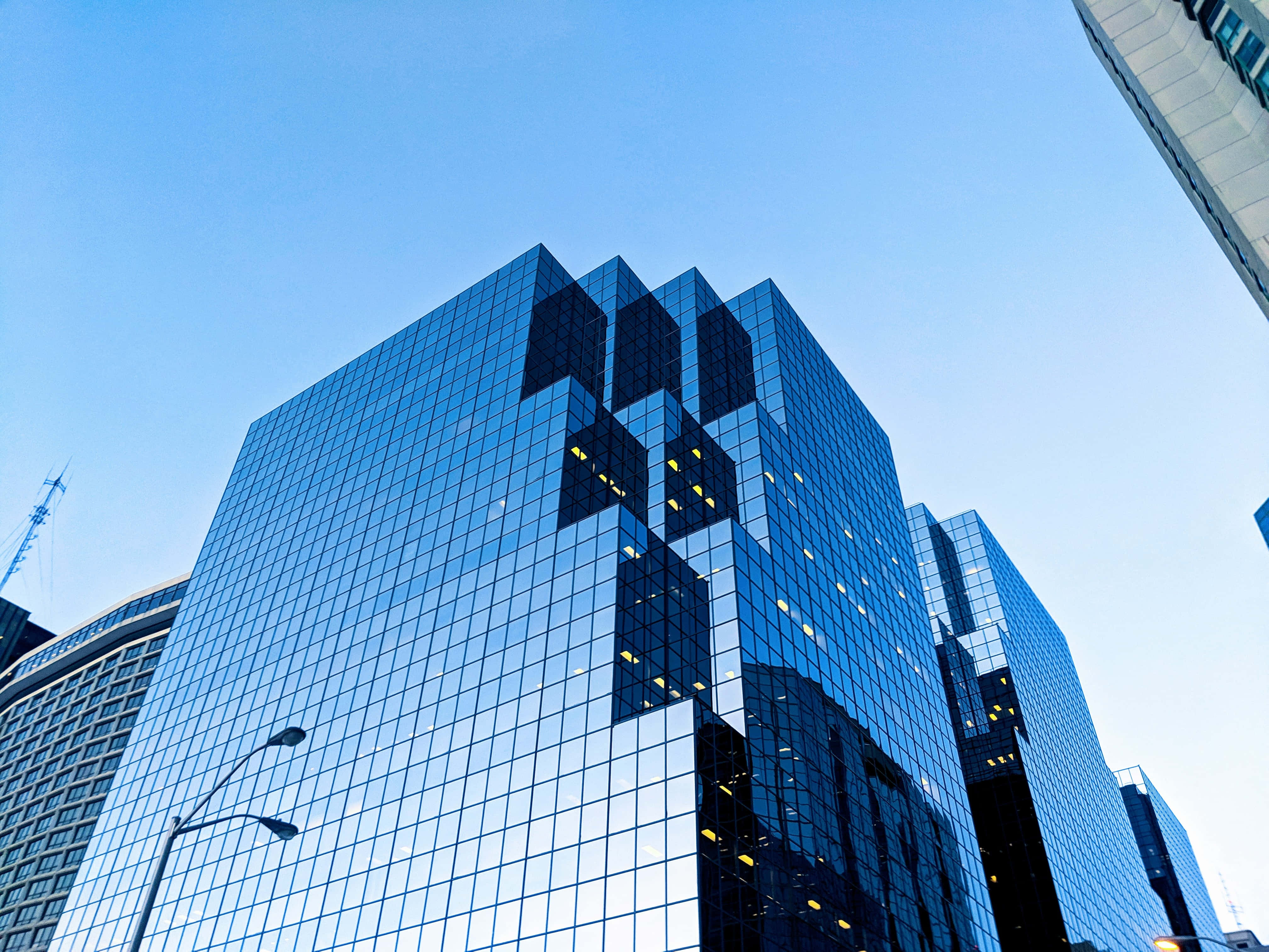 Building 桌布 壁紙 — 低角度拍攝一座高聳的玻璃摩天大樓，反射出清澈的藍天和發光的室內燈光。