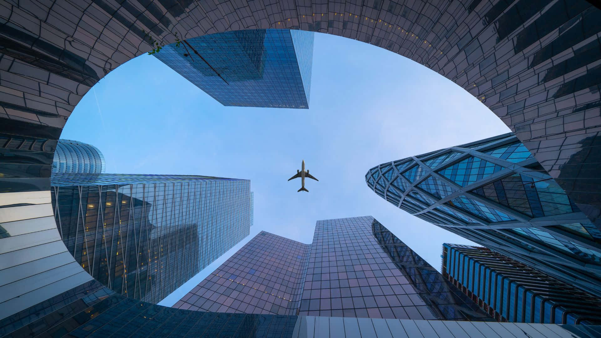 一架飛機在城市中現代玻璃摩天大樓之間飛行。 — 飛機 壁紙
