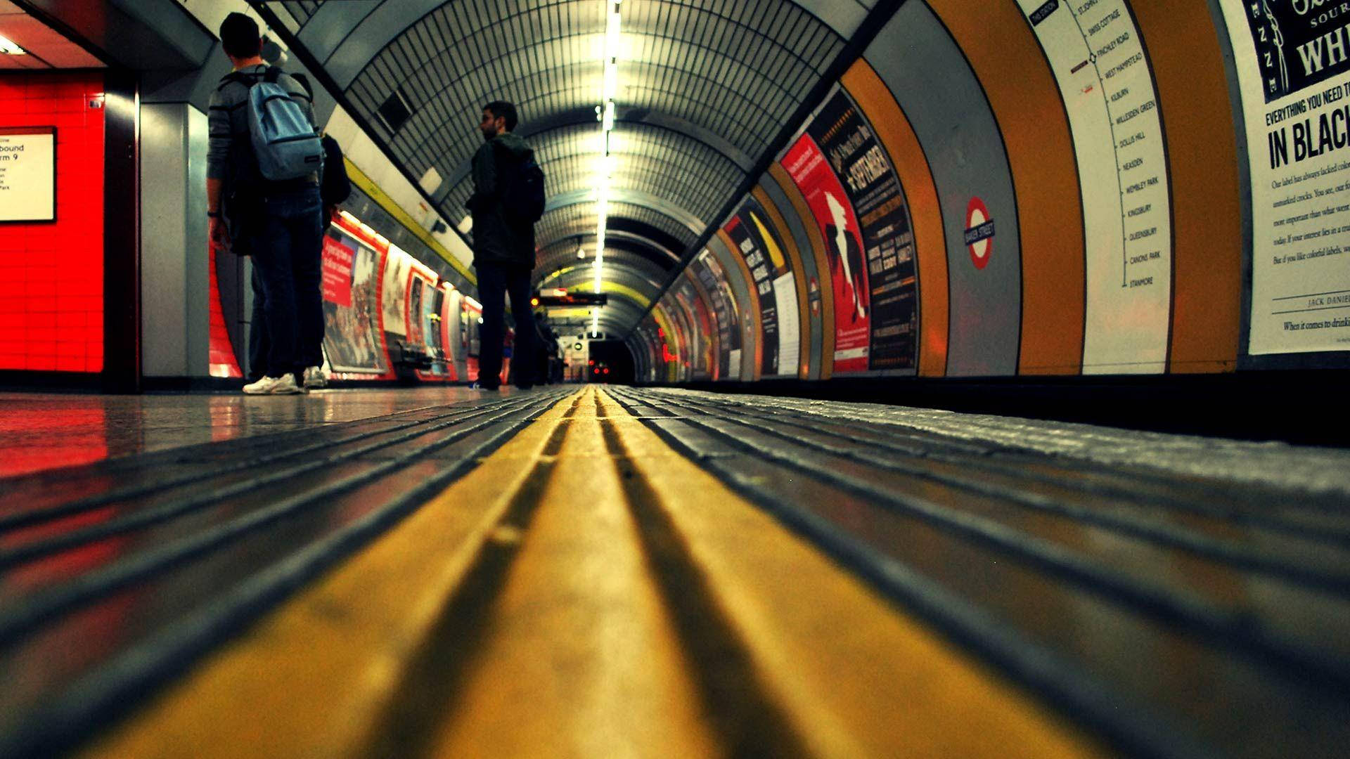 train tunnel 桌布 壁紙 — 低角度拍攝彎曲的地鐵月台，兩人在明亮的螢光燈下站在火車附近。
